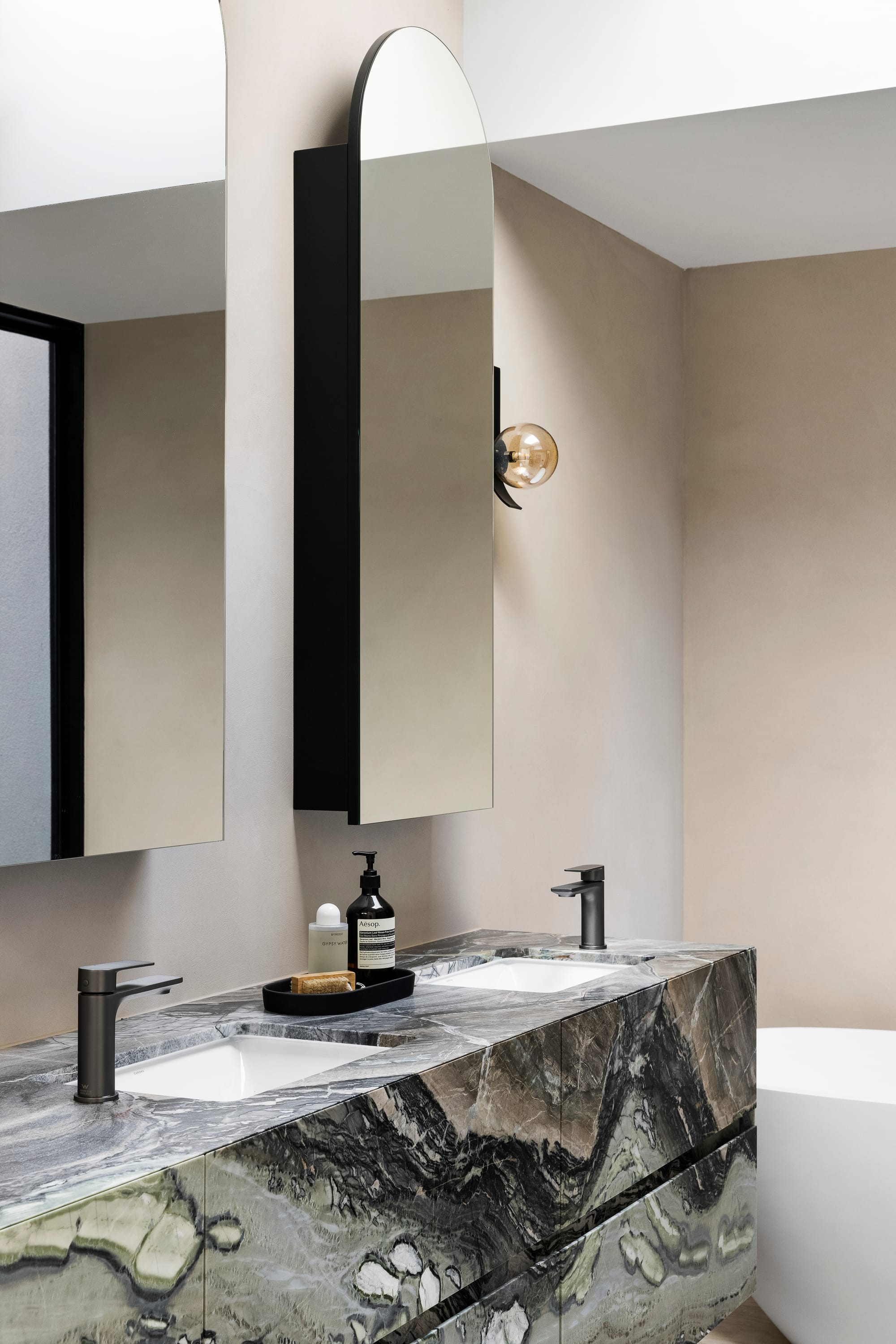 Goldsmith Residence by C.Kairouz Architects. Photography by Spacecraft. Green marbled stone island bench with matching white sinks and black tapware. Tall arched mirrors. 