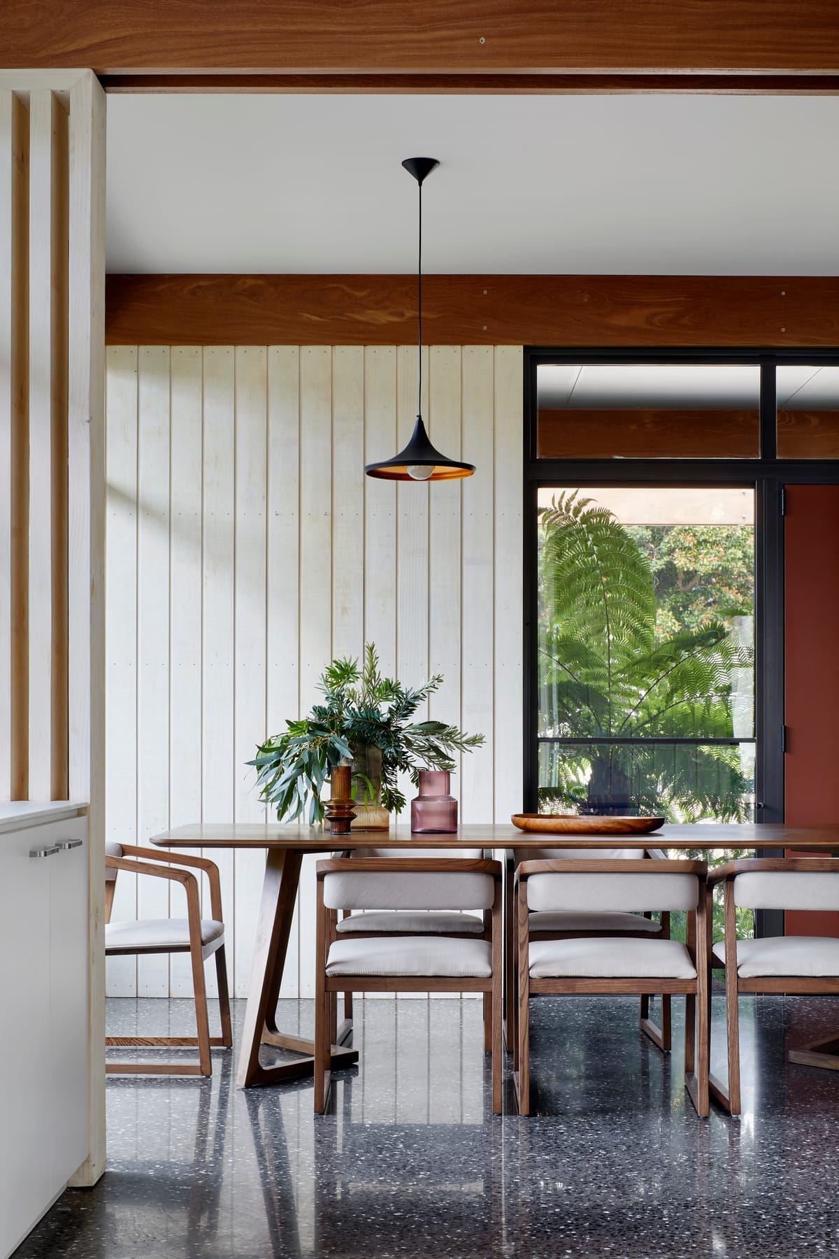 Mt Eliza House by BENT Architecture. Photography by Tatjana Plitt. Interior living space with polished concrete floors, large cream jute rug and central stone fireplace. Large windows on back wall of room overlook exterior gardens. 