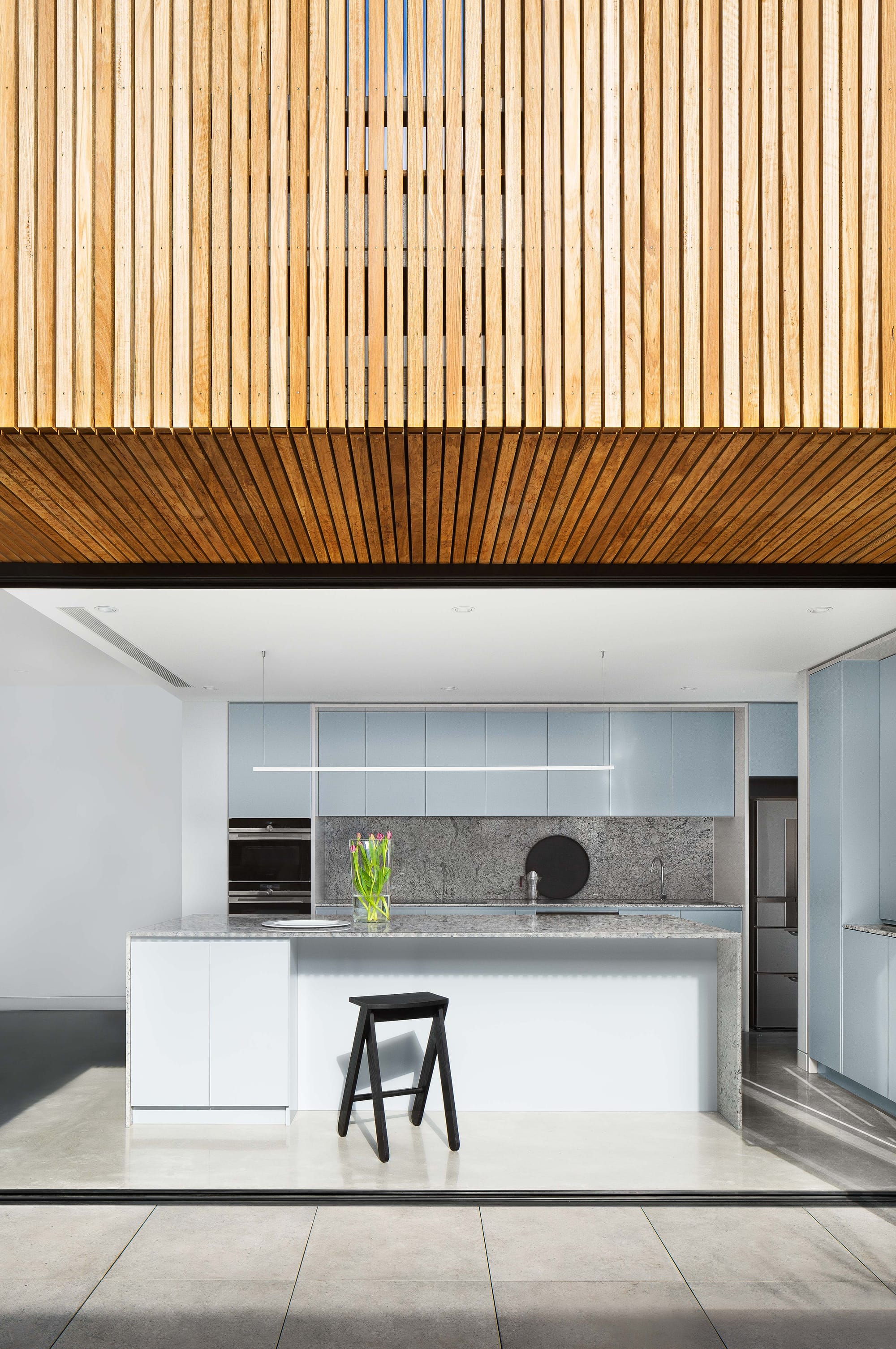 A shot from the outside looking into the white and light blue kitchen with a glimpse of the timber cladding above