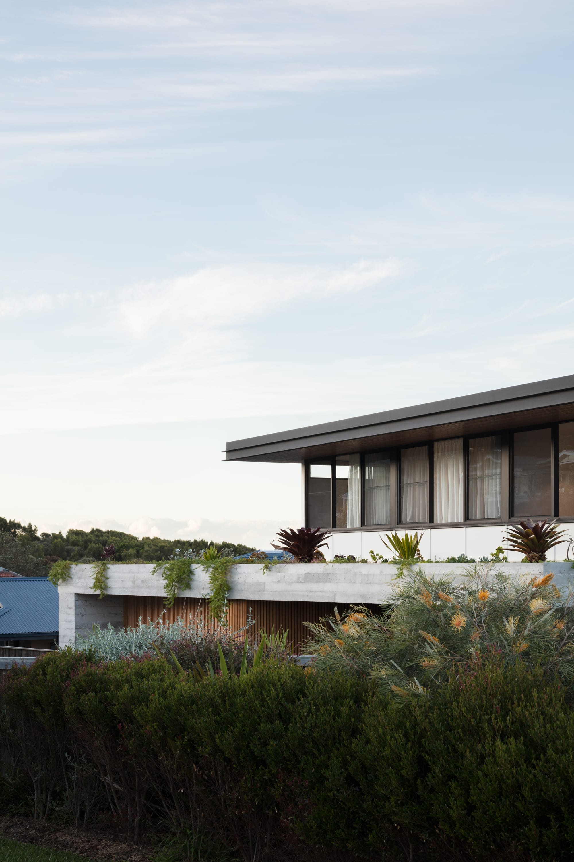 Grandview House by Ian Bennett Design Studio. Photography by Clinton Weaver. Side view of house with concrete bottom floor and windows on upper level. Plants growing over concrete portion of building. 