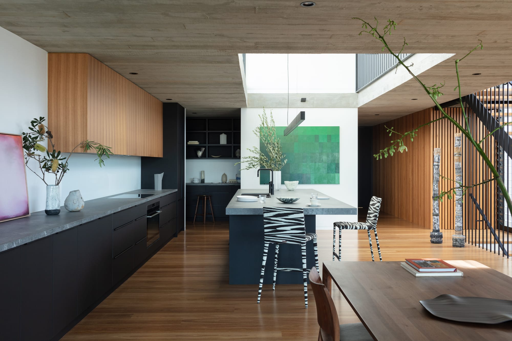 Grandview House by Ian Bennett Design Studio. Photography by Clinton Weaver. Open plan kitchen with timber floors, black cabinetry and concrete-look countertops. Zebra print bar stools. 