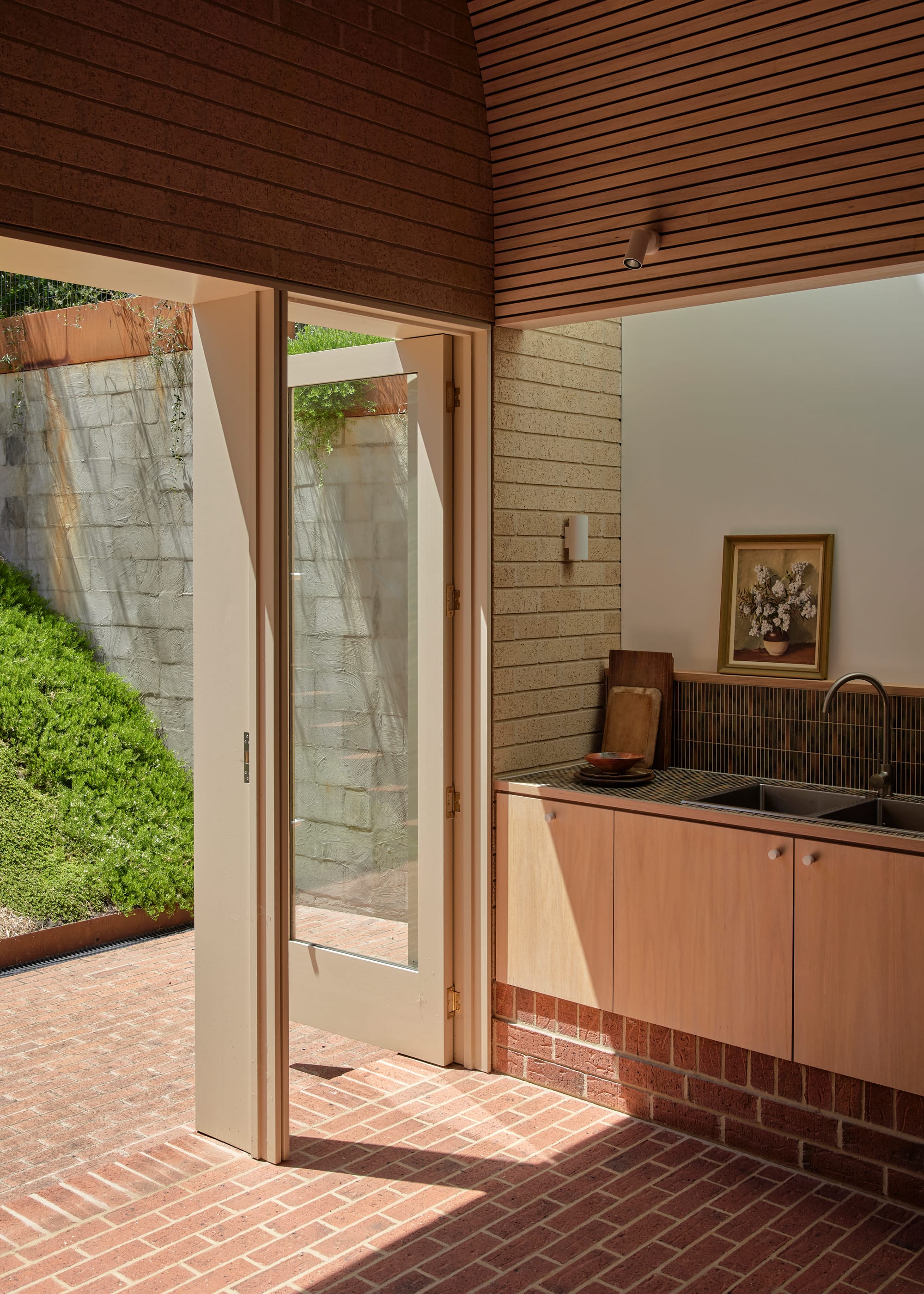 Harriet's House by SO:Architecture. Photography by Sean Fennessy. Tasmanian Oak veneer kitchen cabinets. Folding glass doors open up onto steep back garden. Brick floors and walls.