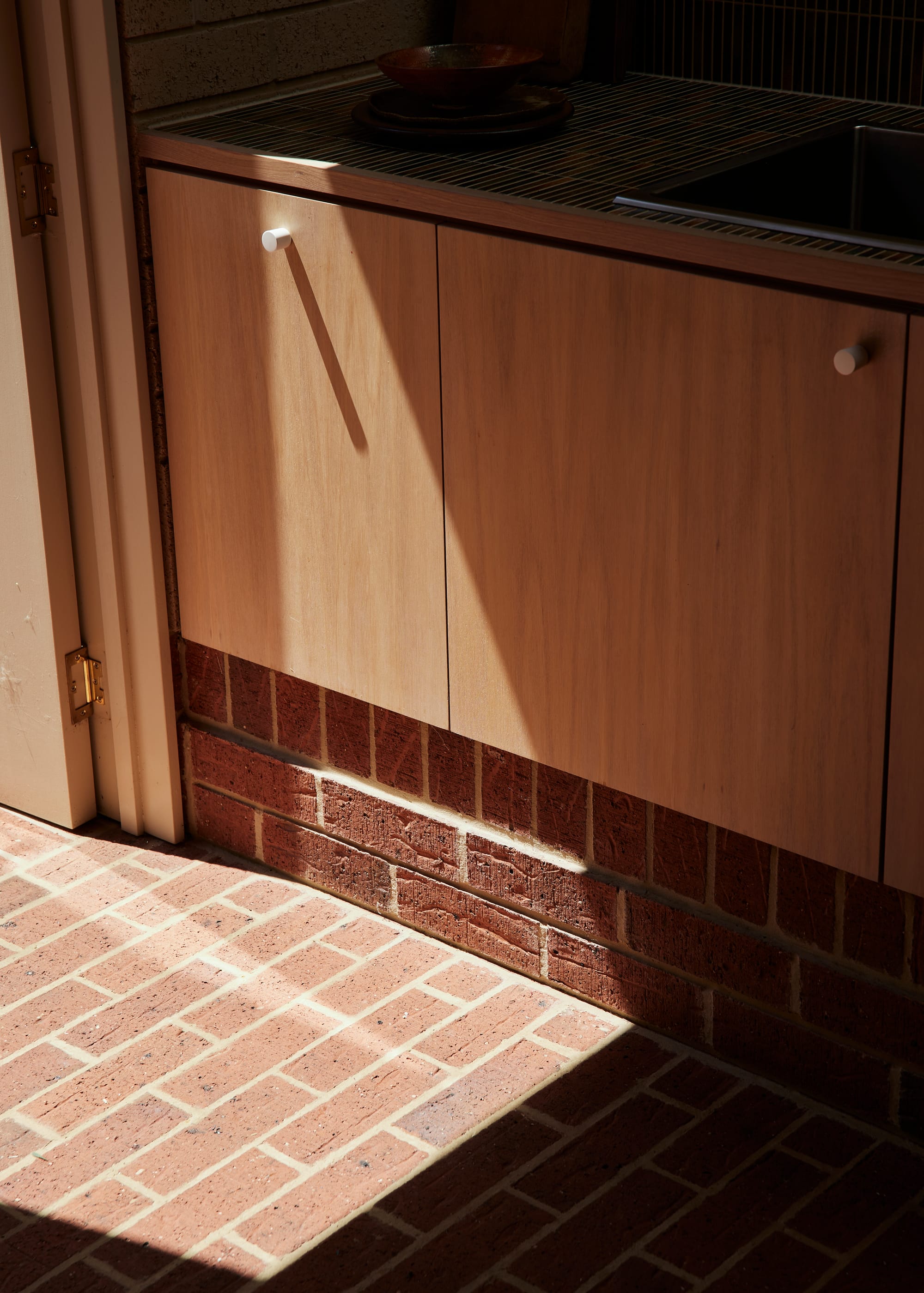 Harriet's House by SO:Architecture. Photography by Sean Fennessy. Close up shot of brick flooring meeting brick kickboard underneath Tasmanian Oak veneer cabinetry.