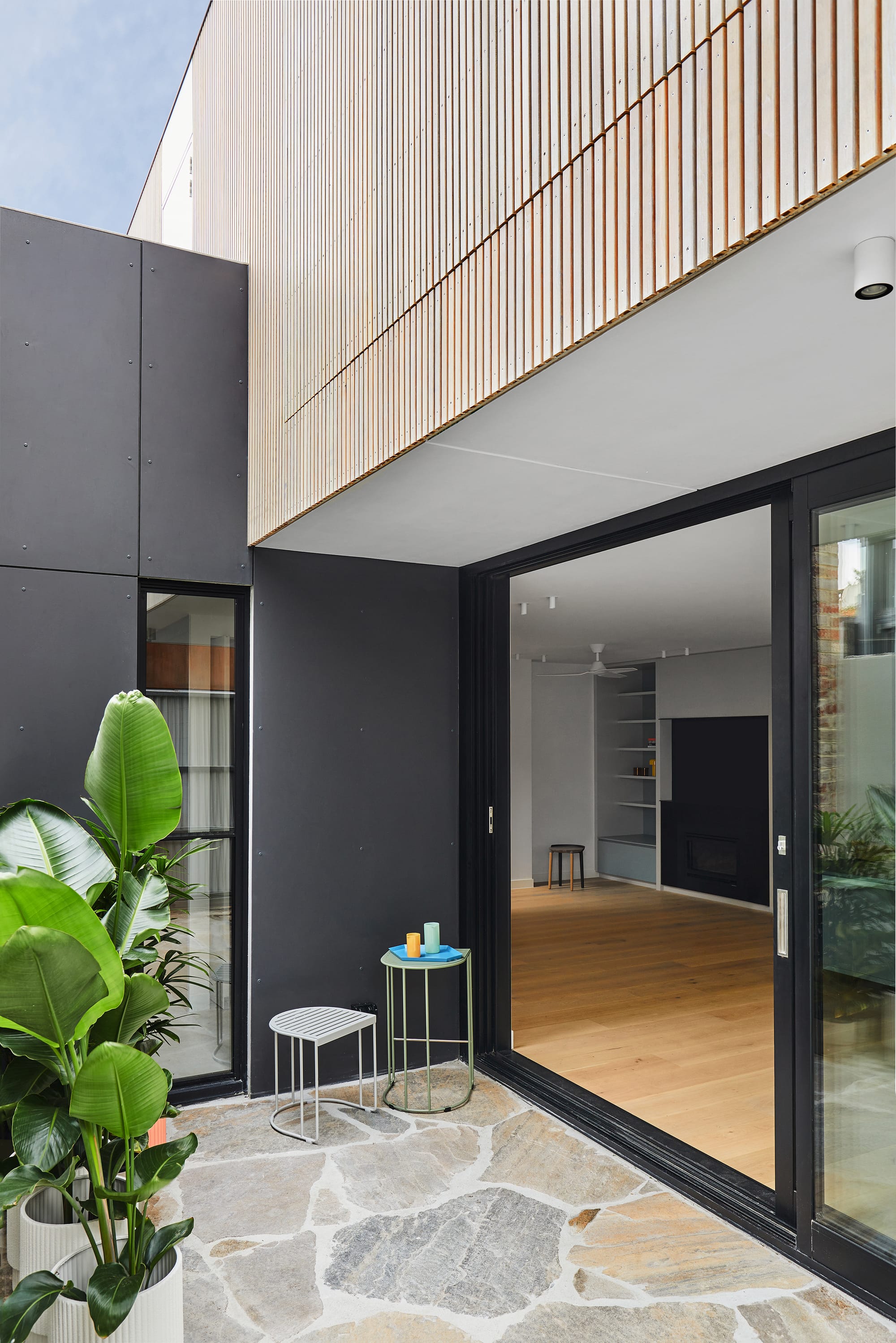 The Full Monty by FYC Architects. Photography by Stephanie Rooney. Courtyard space with stone pavers and black walls opens of interior living space with timber floors. 