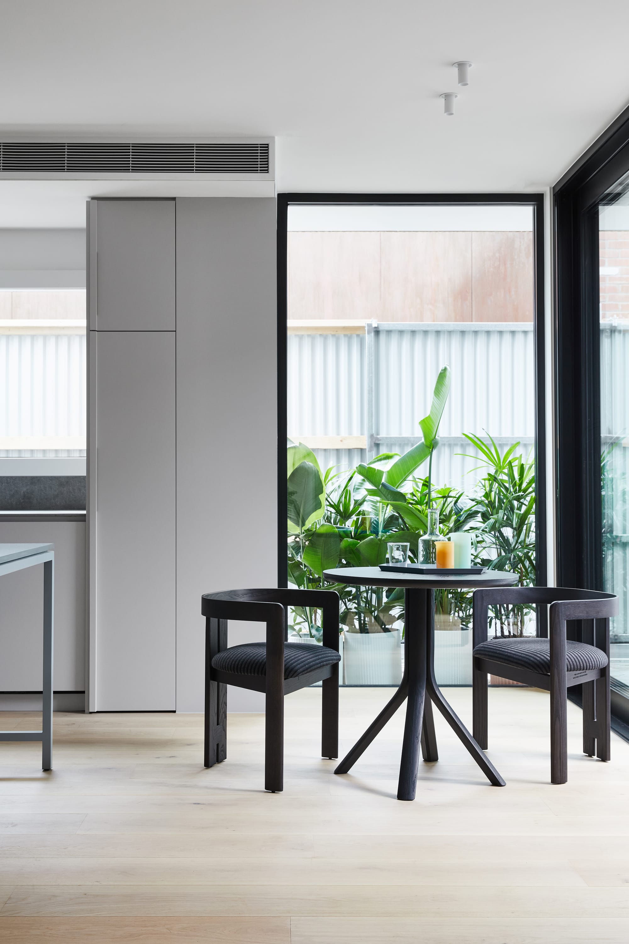 The Full Monty by FYC Architects. Photography by Stephanie Rooney. Kitchen and dining space with pale timber floors, a black round dining setting and floor-to-ceiling windows. 