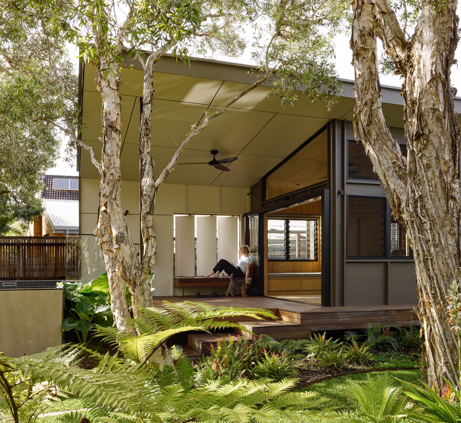 Rear verandah of home with slanted roof and louvered openings in white wall. Interior opens onto verandah. 