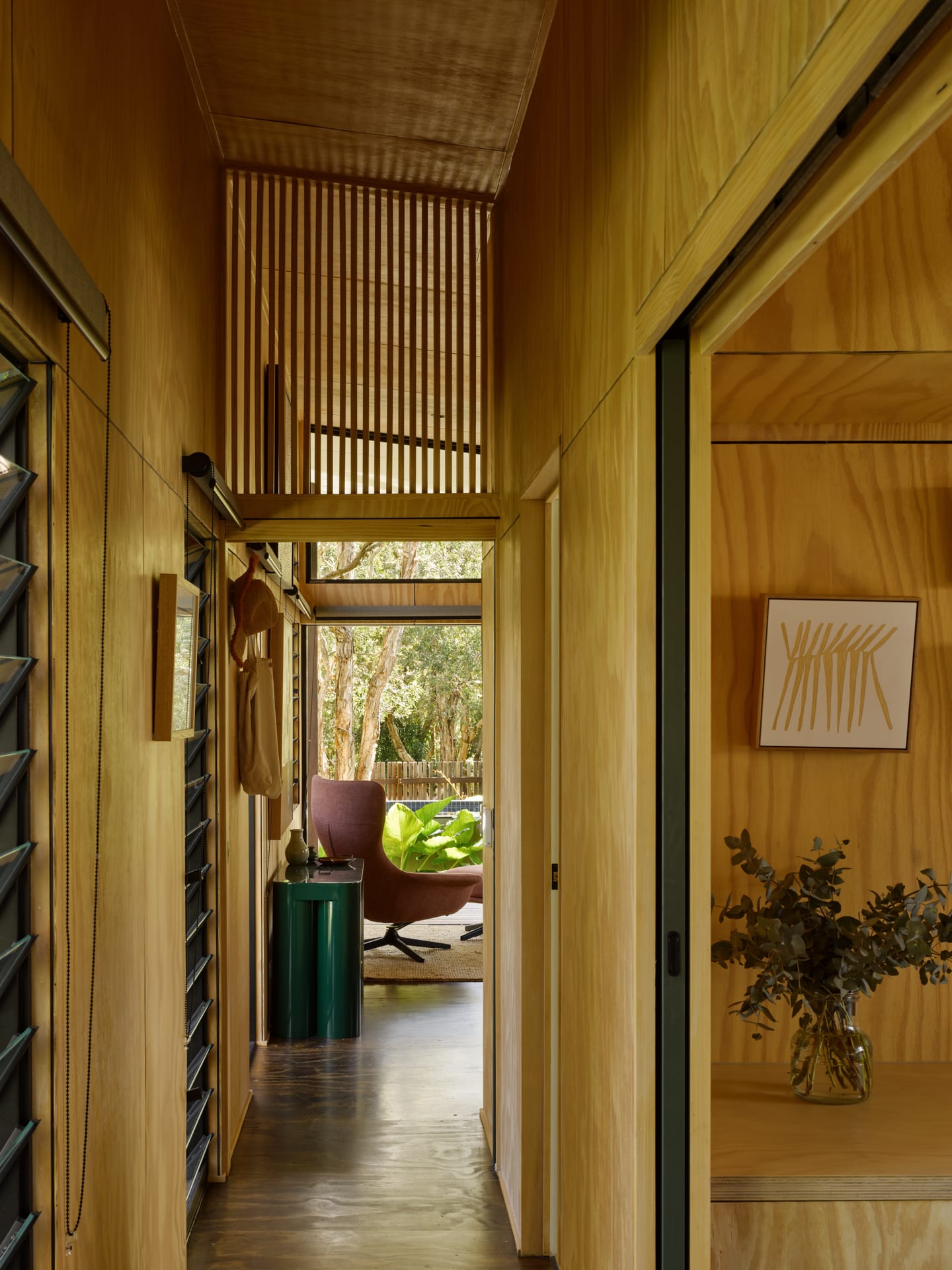 PaperBark Pod by Bark Design. Photography by Christopher Frederick Jones. Interior hallway clad with plywood panels on the walls. Plywood floors. Large windowed opening overlooks dense plantlife.