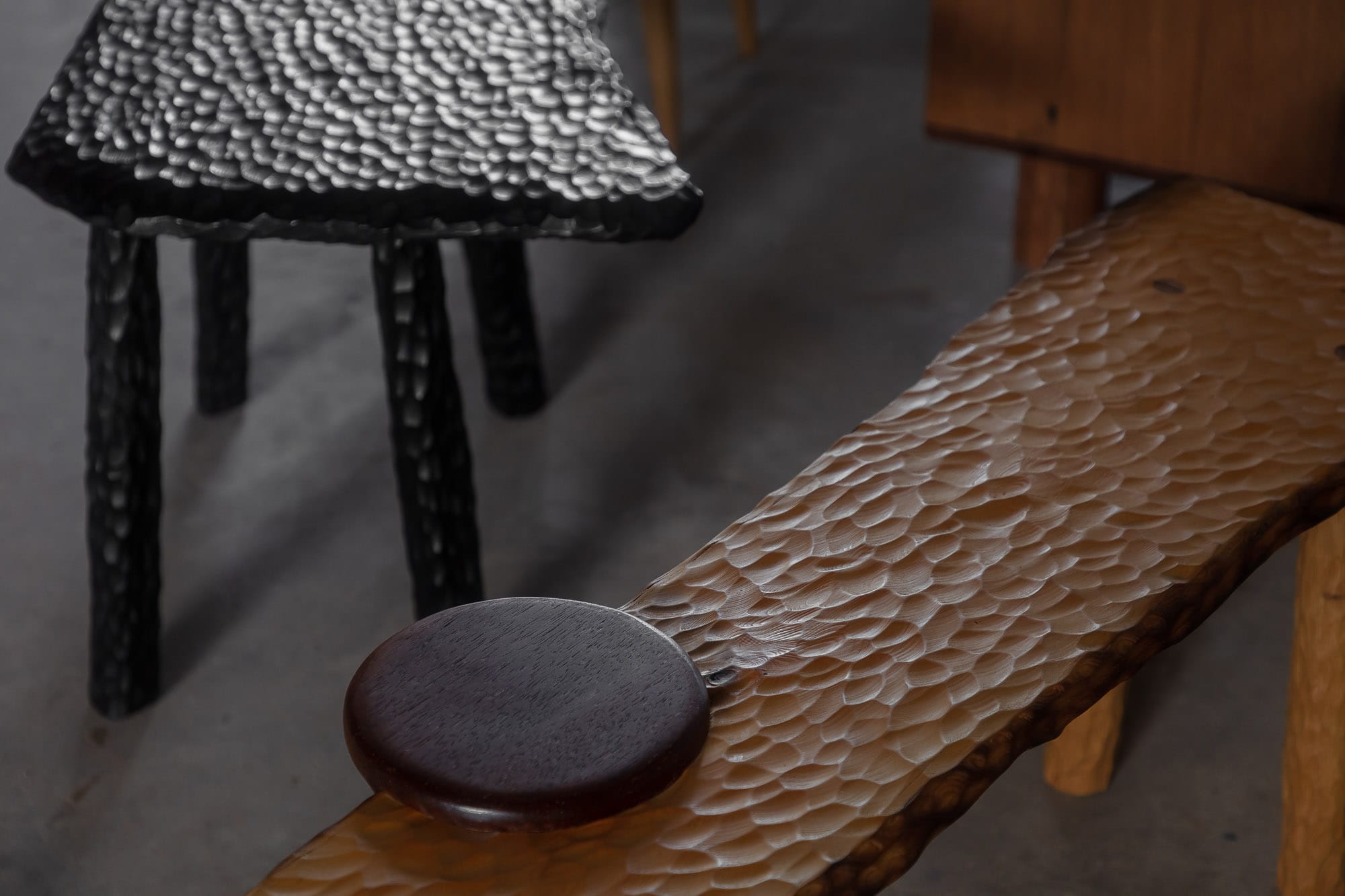 Two Blue Boys. Copyright of Two Blue Boys. Close up image of timber and black benches with carved texture. Circular black decorative plate. 