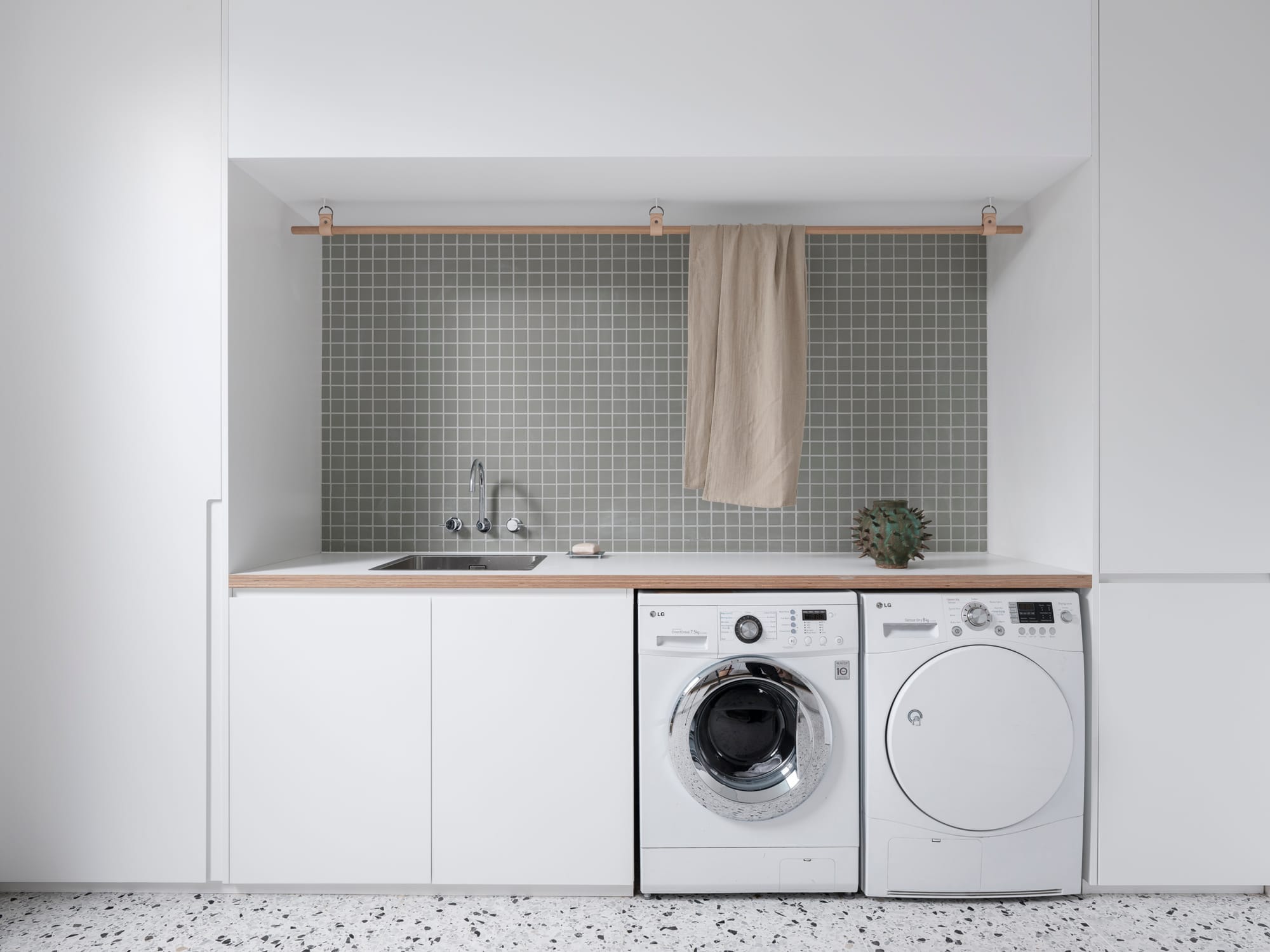 Bellevue House by Carla Middleton Architects. Photography by Tom Ferguson. White laundry cabinetry with sage square tiled splashback. Terrazzo flooring. Timber rail floating above benchtop. 