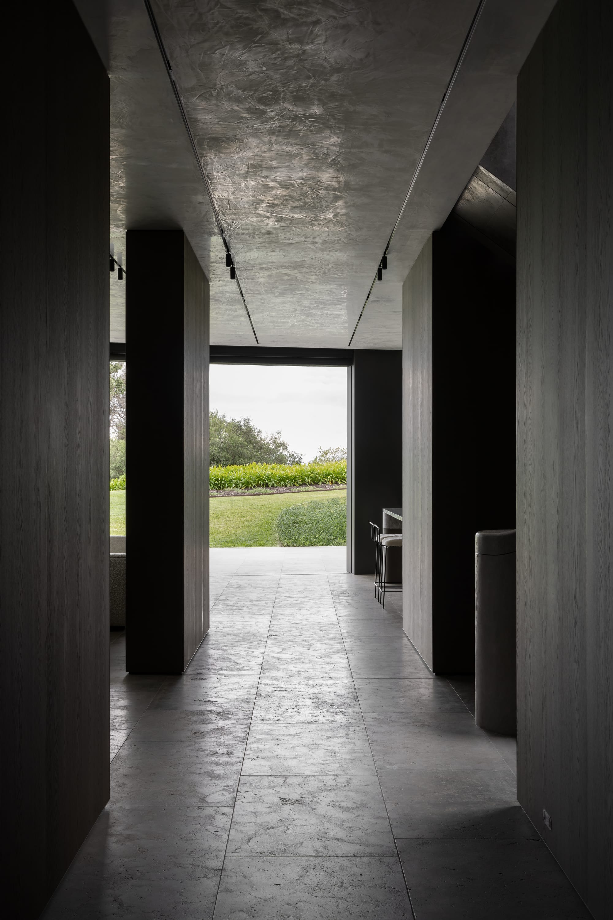 Cliff House by Finnis Architects. Photography by Timothy Kaye. Hallway with garden views through floor-to-ceiling windows at the end. Stone floors and timber veneer walls. 