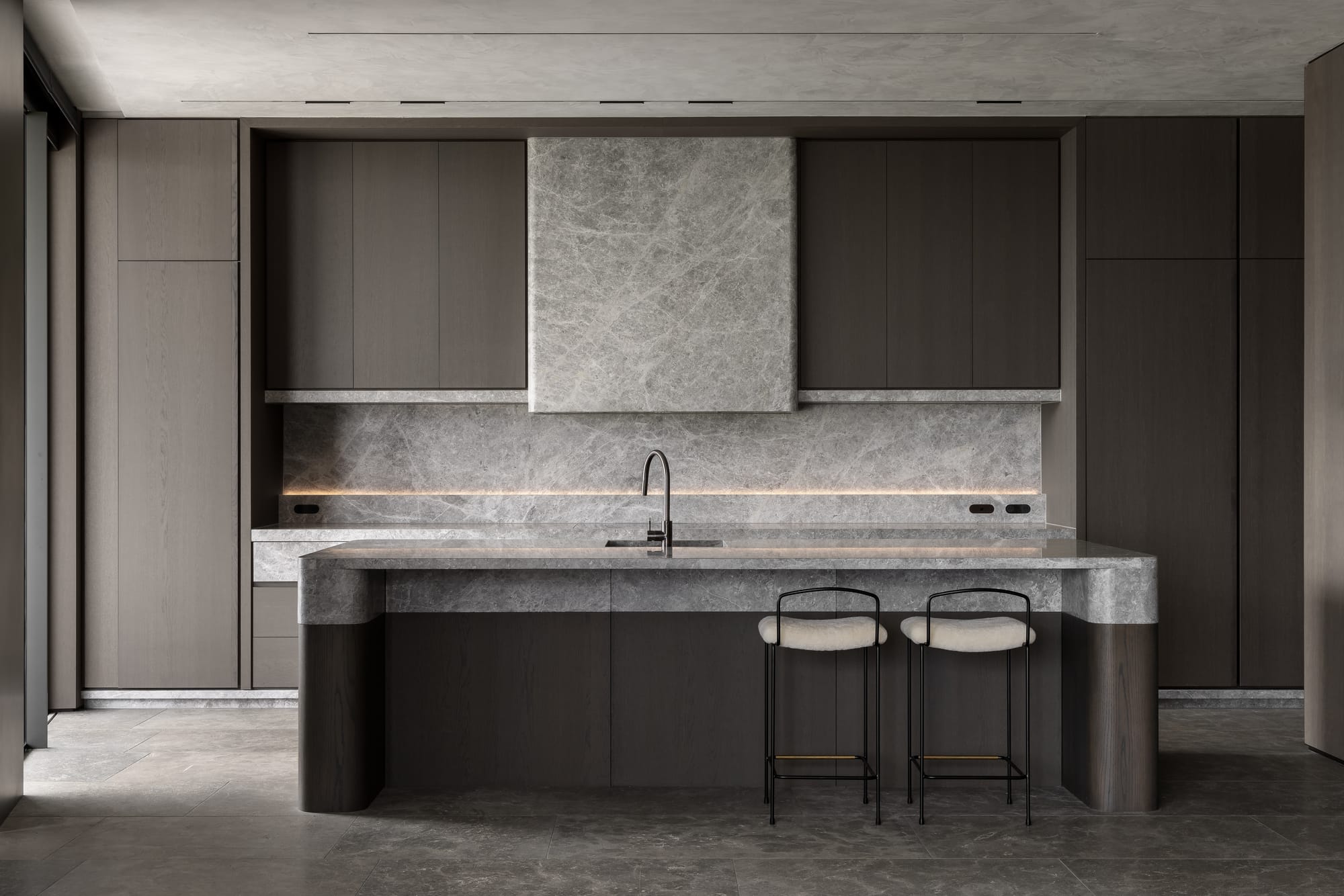 Cliff House by Finnis Architects. Photography by Timothy Kaye. Kitchen with dark timber veneer cabinetry and stone countertop, splashback and rangehood. Stone floors and cement look ceiling. 