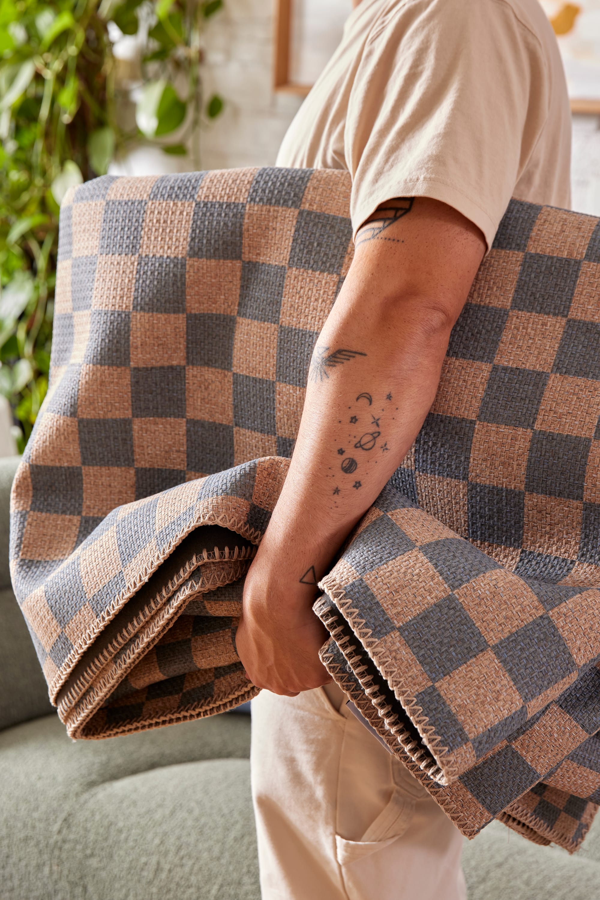 Double Rugs New Check Collection. Photographer: Jacqui Turk. Close up of a tattooed arm holding a blue and cream checkered rug under their arm. 