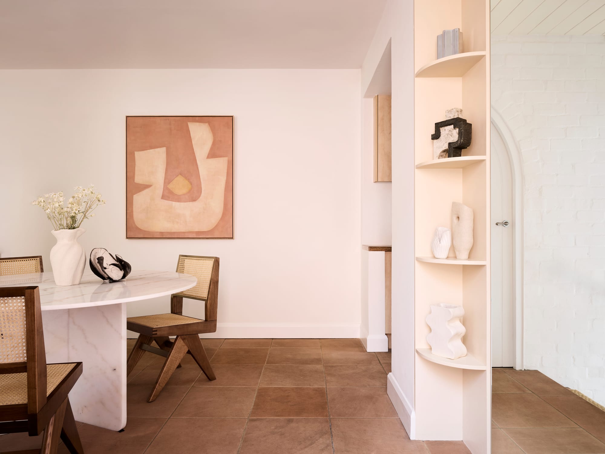 Chapel House by FURNISHD. Photography by Alicia Taylor. Dining room and hallway. White walls and paved floors. White marble dining table and rattan dining chairs.