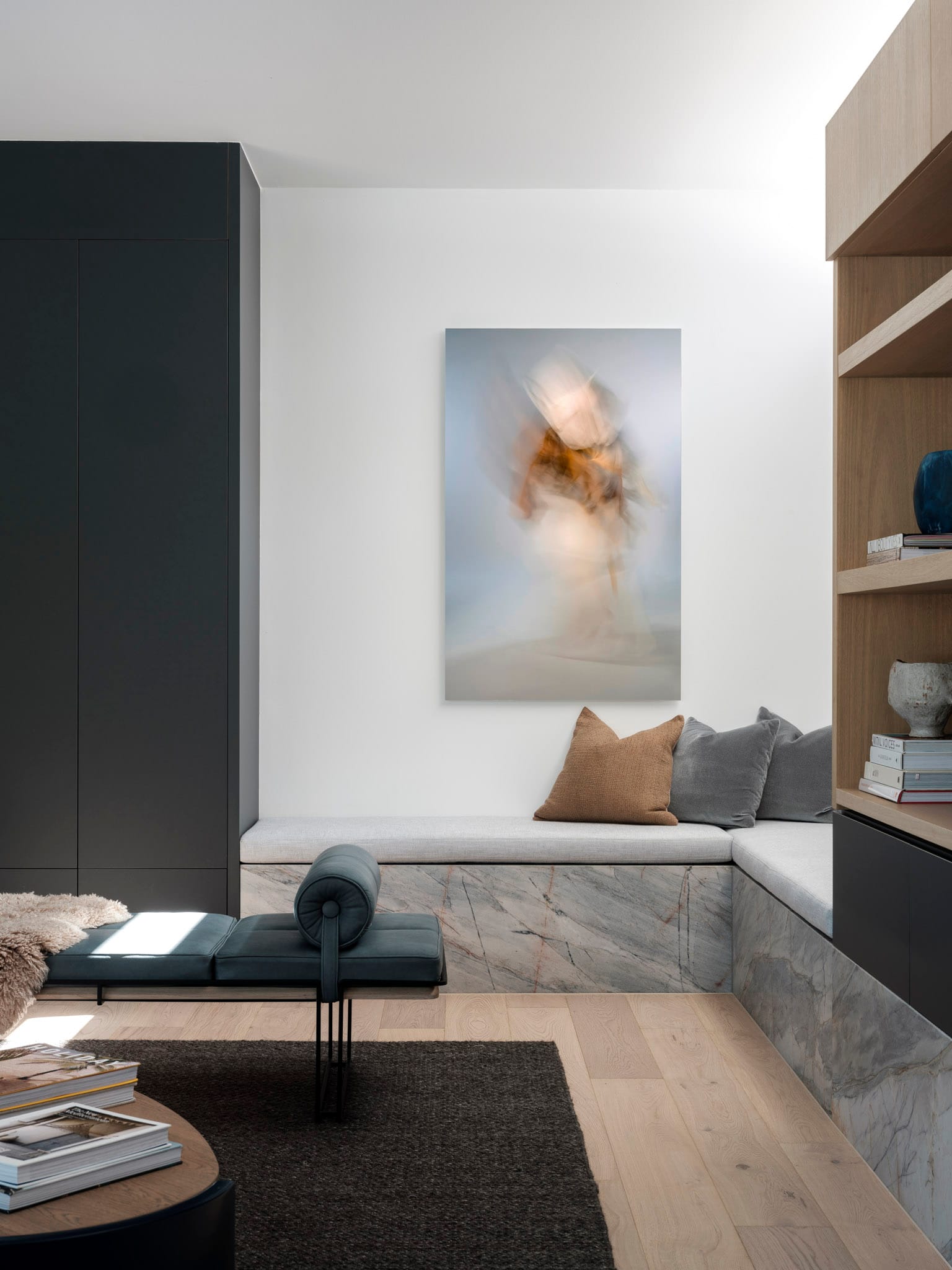 Kasa Byron Bay. Photography by Tom Ferguson. Living space with built in stone bench seat with grey cushion seat. Timber floors and charcoal rug. Charcoal and timber joinery. 