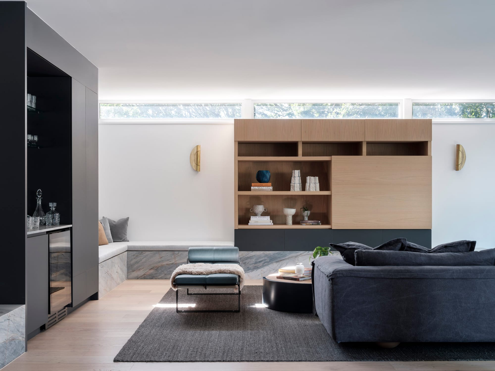 Kasa Byron Bay. Photography by Tom Ferguson. Living room with navy couch and stone bench seat. Timber and black cabinetry. White walls with gold wall sconces. 