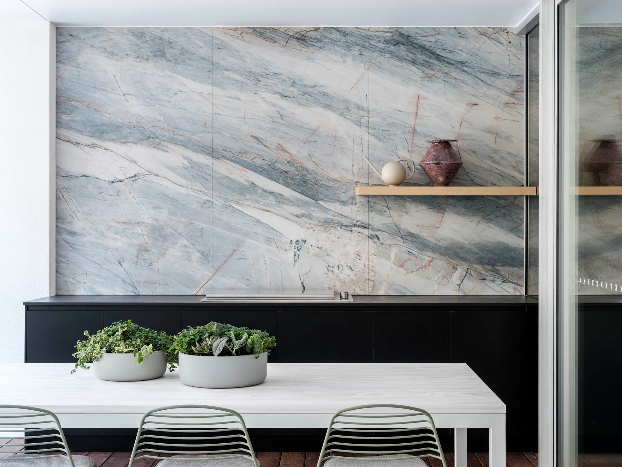 Kasa Byron Bay. Photography by Tom Ferguson. White outdoor dining setting. Black outdoor kitchen with stone splashback. Timber floating display shelf. 