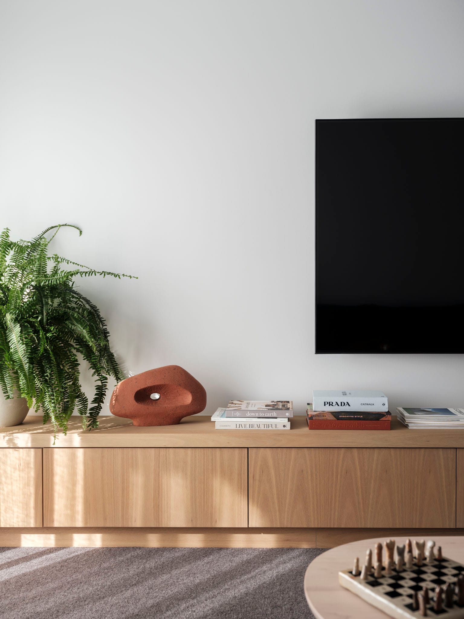 Kasa Byron Bay. Photography by Tom Ferguson. Living room timber joinery tv unit. Grey carpets and white walls. Books stacked on unit. 