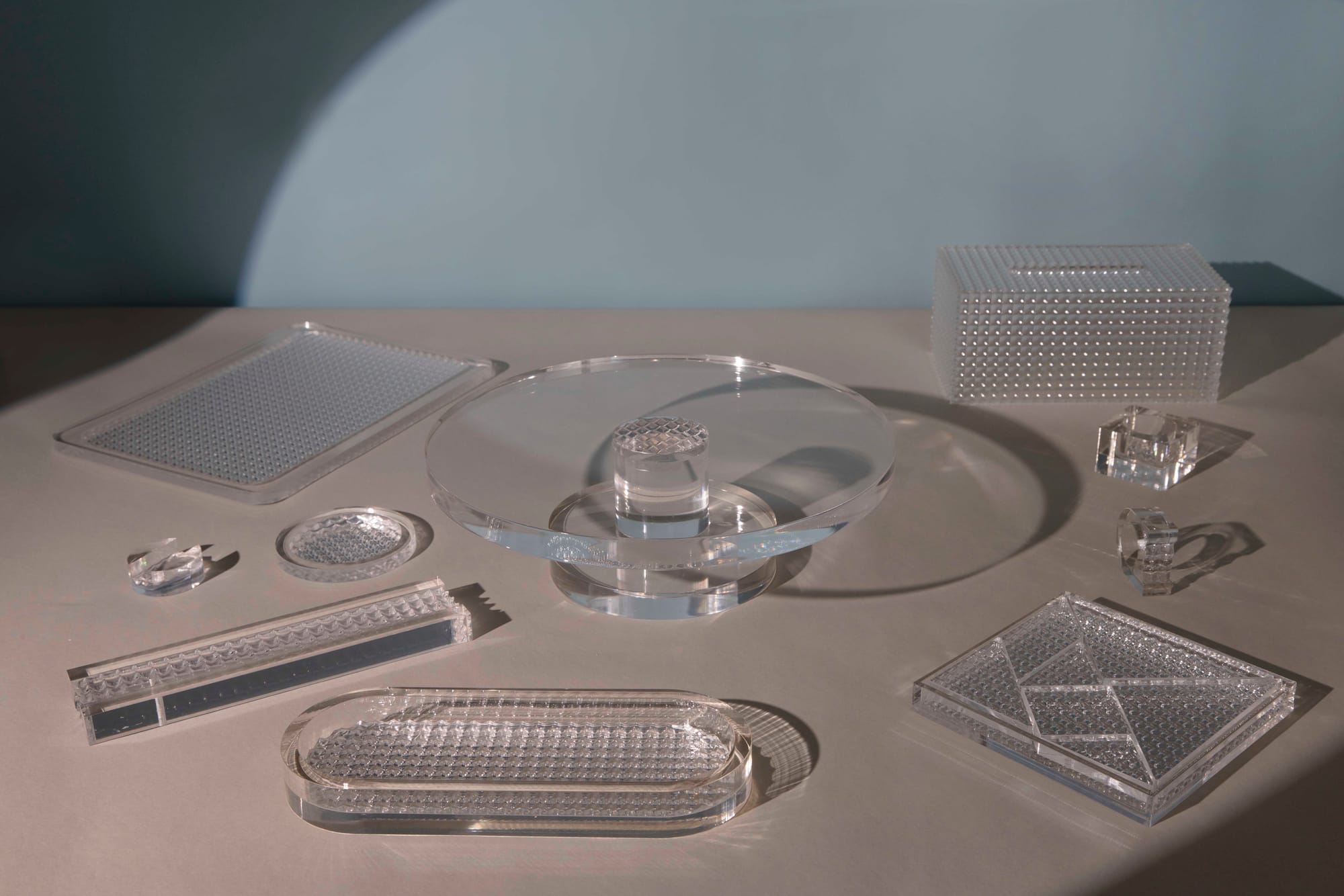 Table Service by Studio Shand. Photography by Darren Luk. Arrangement of various trays and platters. All made of thick, clear material with spiked texture in various areas. 