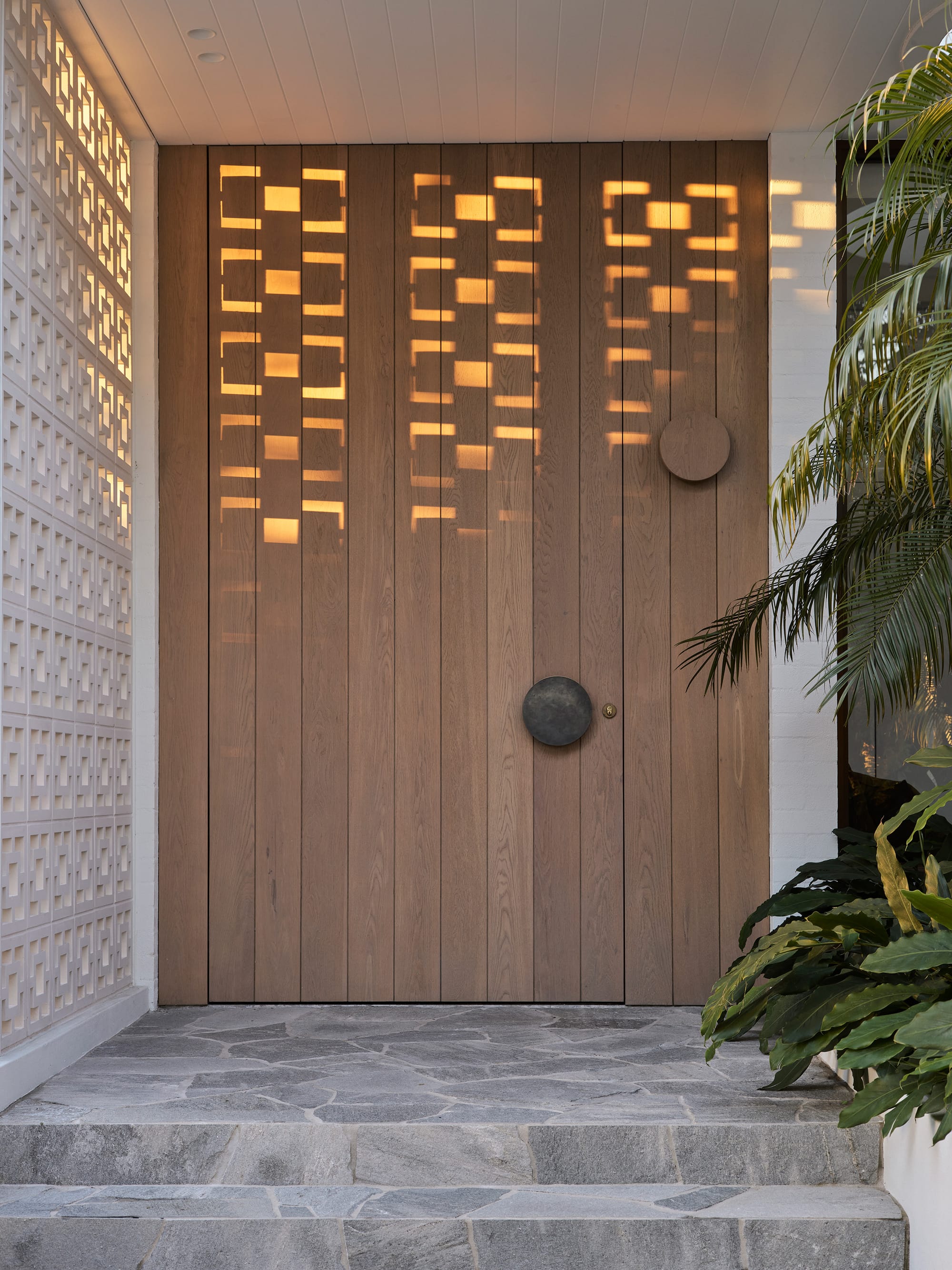 Warren House by CM Studio. Photography by Nic Gossage. Timber front door with round statement door handle in dark metal. White breezeblocks wall to let. Stone pavers on floor.