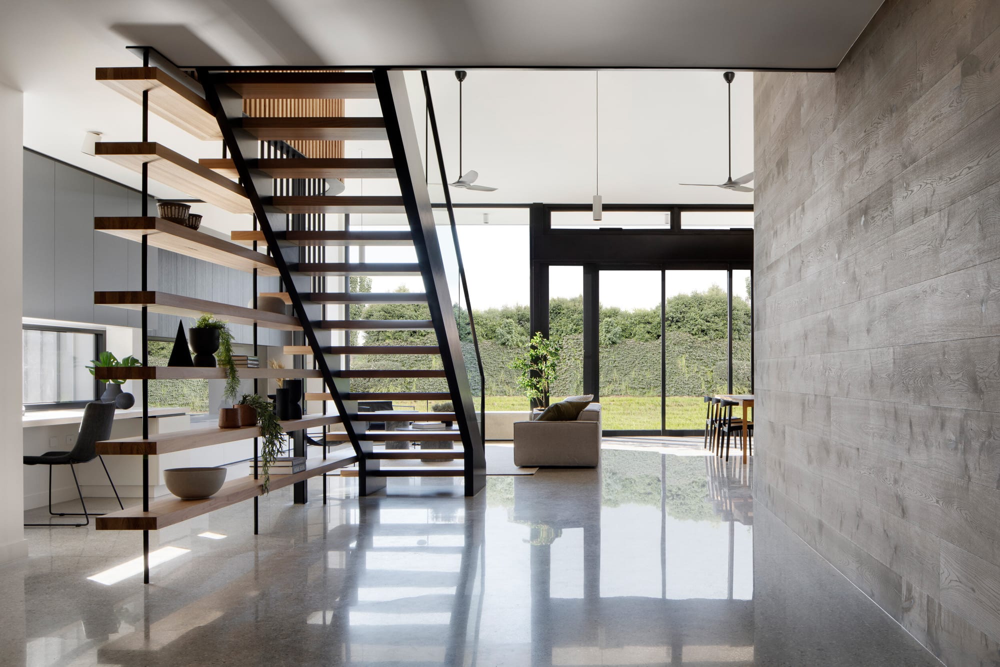 Kenny Street Huse by Chan Architecture. Photography by Tatjana Plitt. Open plan kitchen and living space with polished concrete floors and central staircase. Wall heigh windows and doors overlook open green grass in backyard. 