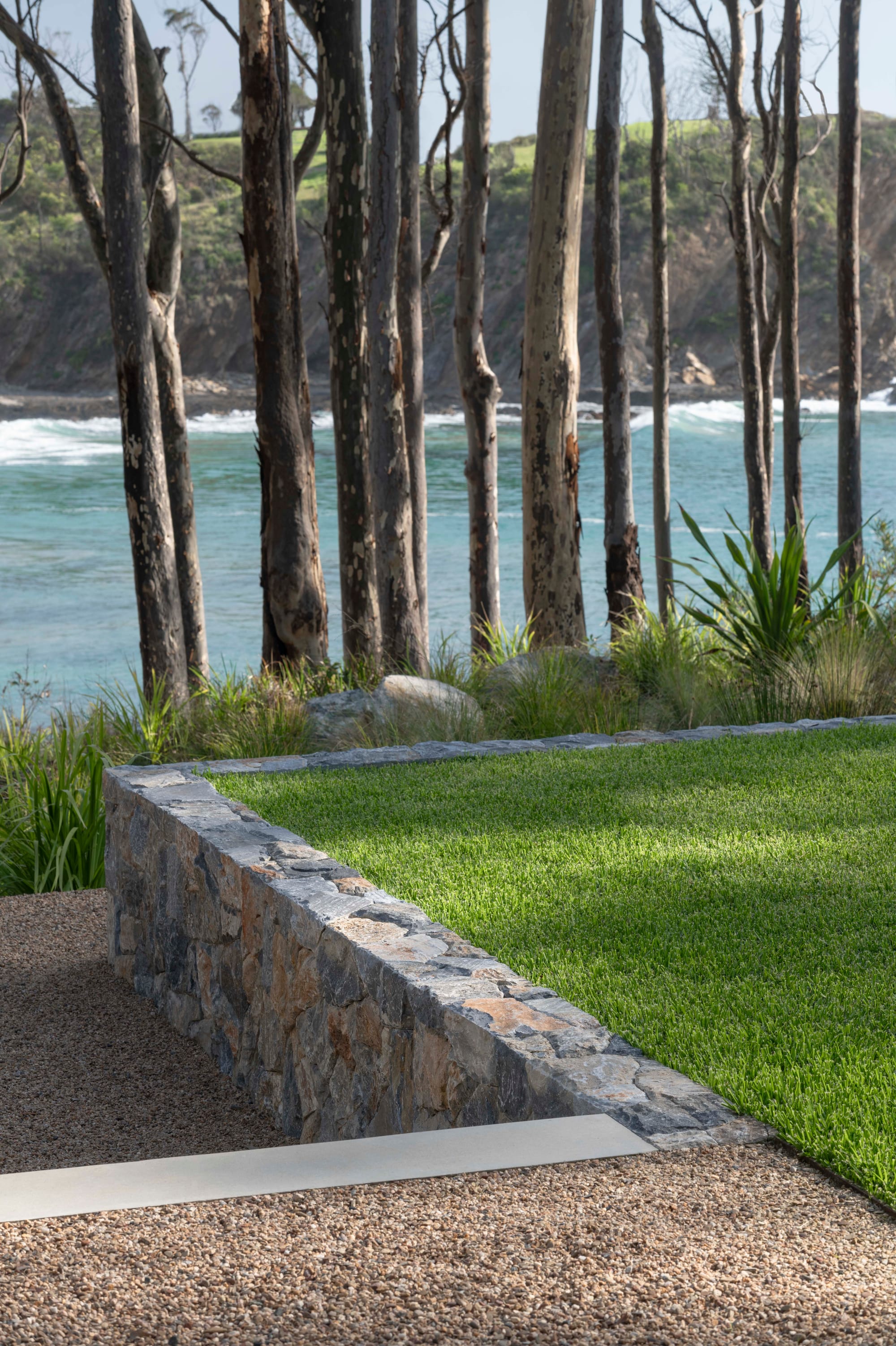Bracken by Secret Gardens. Photography by Nicholas Watt. Detail of stone retaining wall meeting concrete step, green grass and crushed stone path.