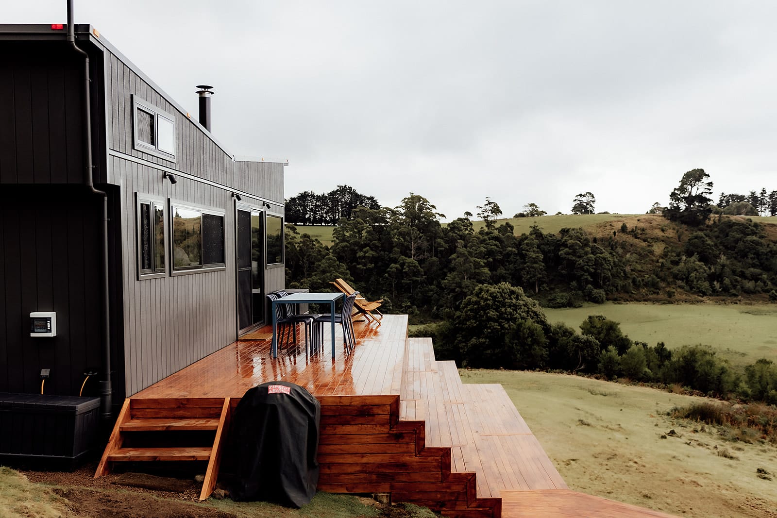 Candlebark Ridge. Copyright of Candlebark Ridge. Large timber deck extending off black timber clad home. Green hilly paddocks surrounding property. 