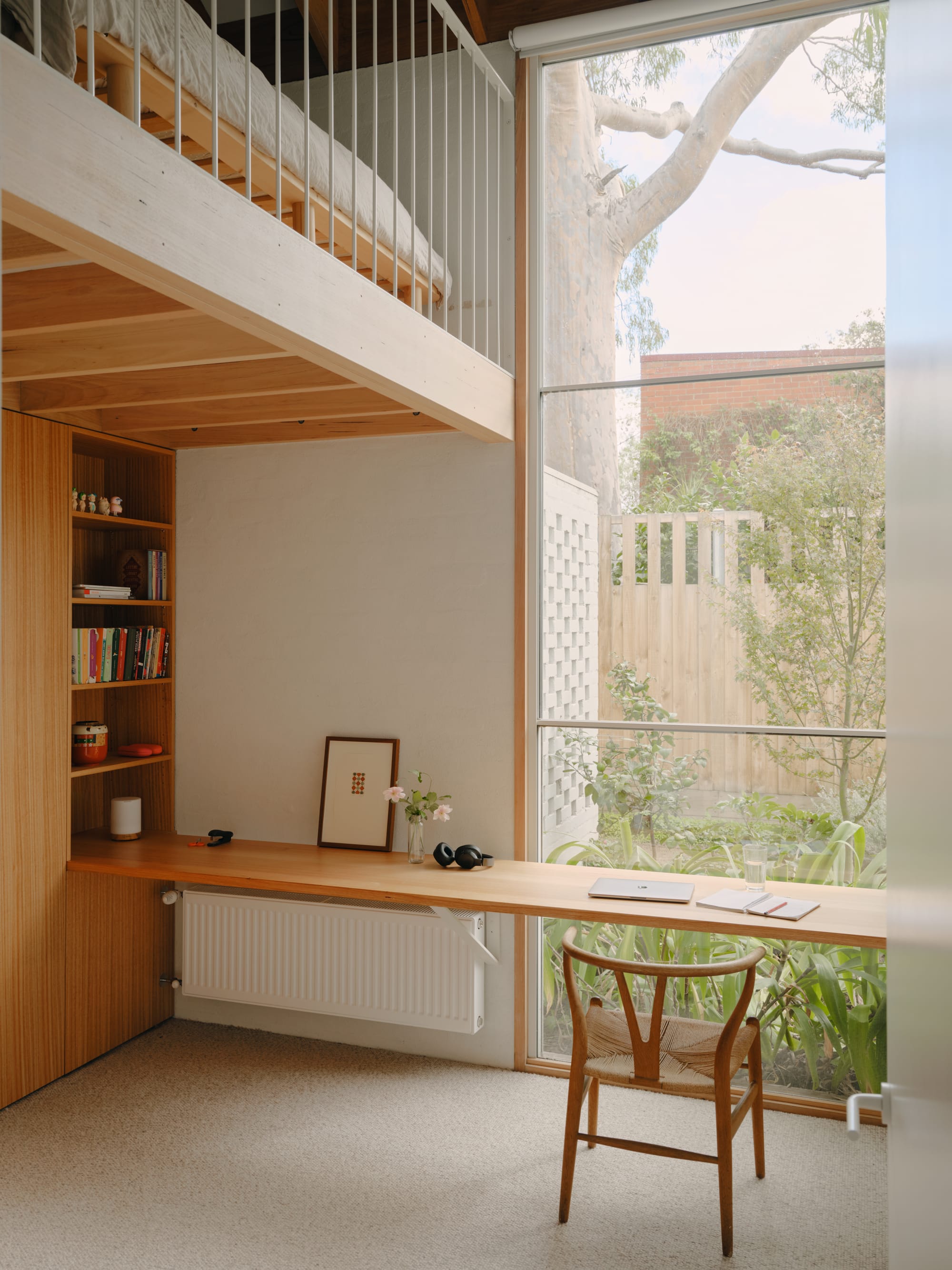 Corymbia by Karen Abernethy Architects. Photography by Tom Ross. Bedroom of residential home with timber joinery wardrobes and floating desk in front of window. Mezzanine level overhead.  Beige carpets and white walls. 