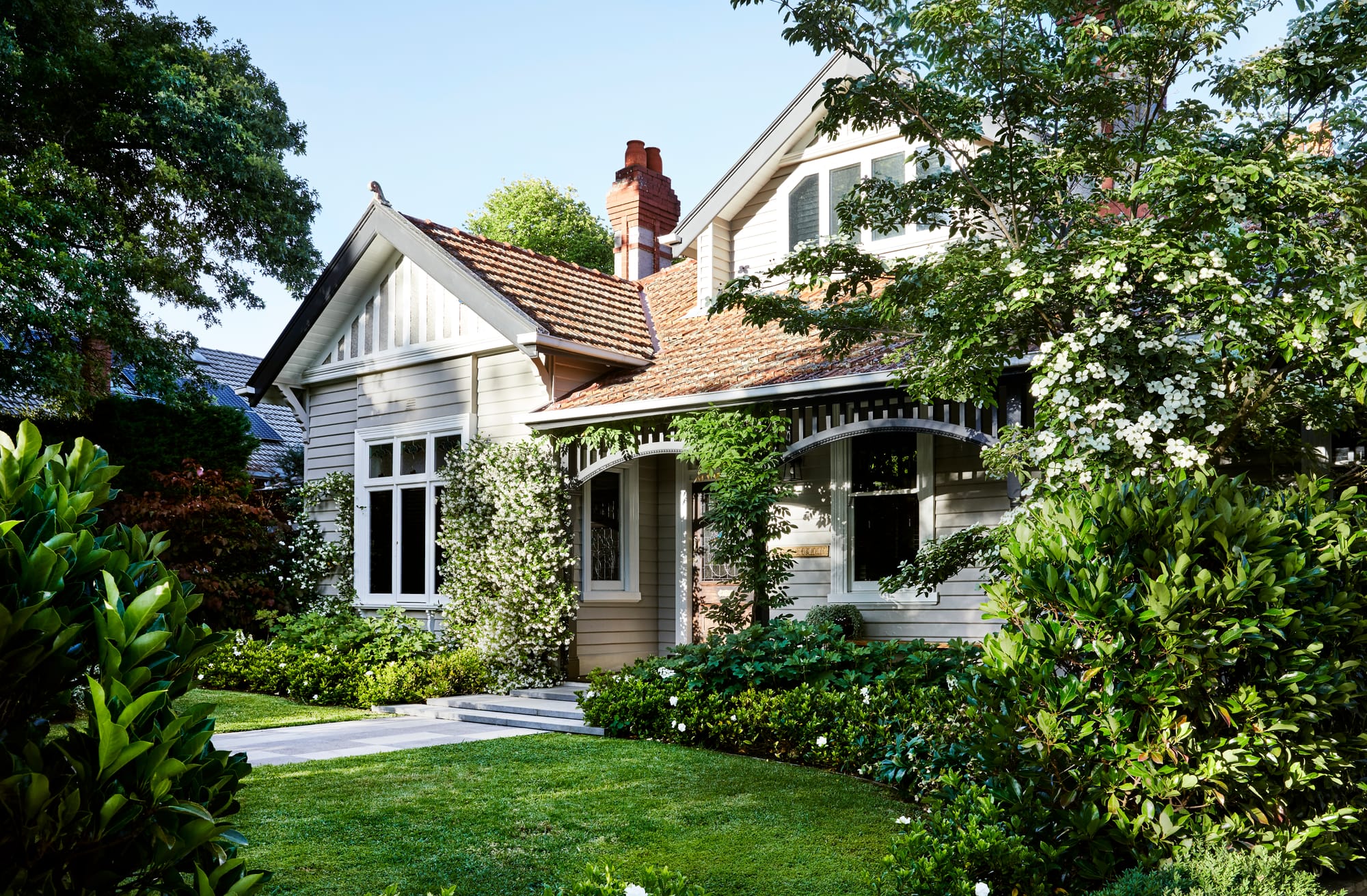 Julie Crowe Landscape Design. Photography by Caitlin Mills Photography. External facade of double-storey clad home with plants growing across verandah. Green front lawn and garden beds. 