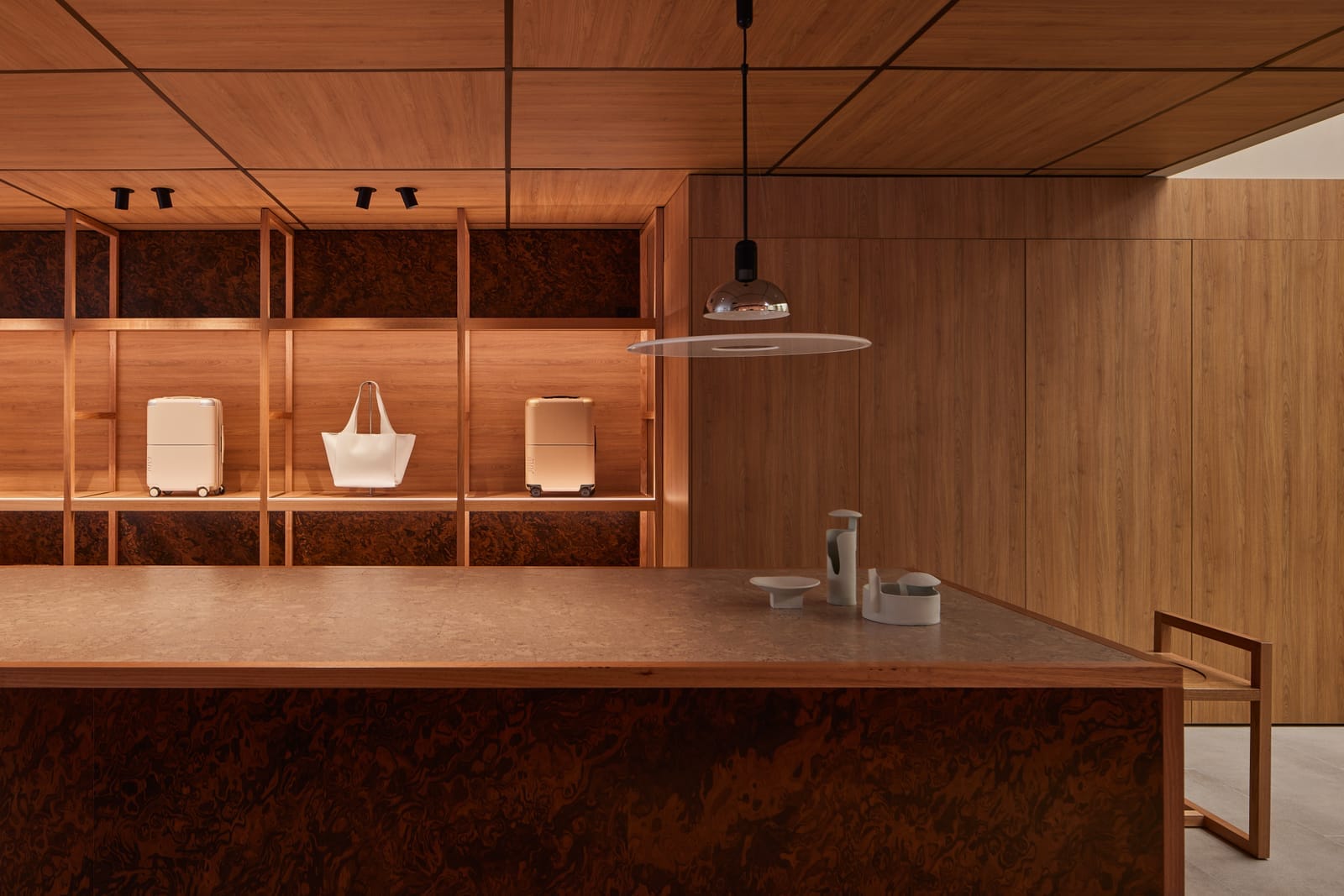 July Store by Acre. Photography by Cieran Murphy. Timber shelving and veneer ceiling. Large timber island bench with mi-century finishes. White and chrome hanging pendant.
