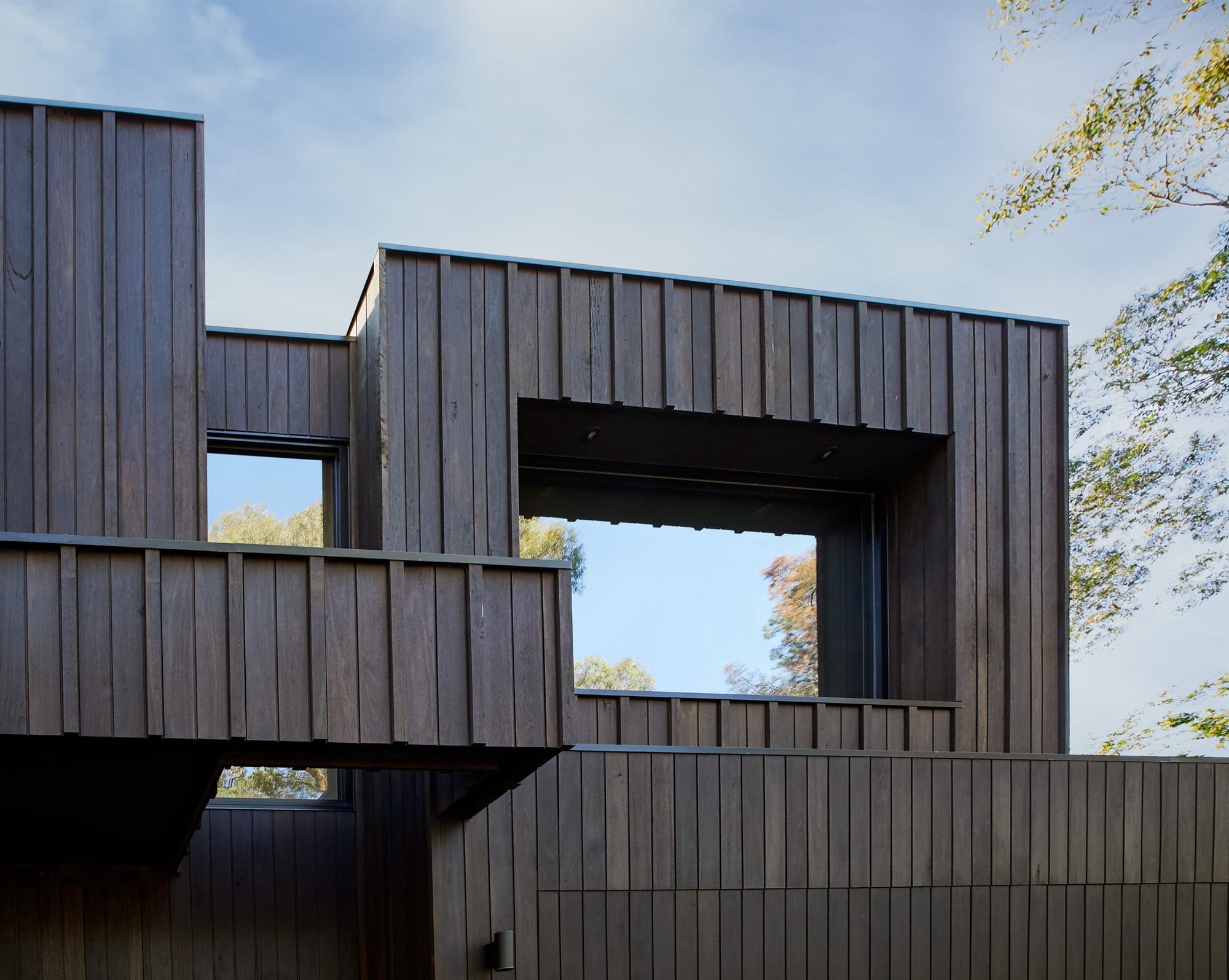 Laurel Grove by Kirsten Johnstone Architecture. Photography by Tatjana Plitt. Inset windows on second floor of contemporary, black timber clad home. Windows reflect gum trees surrounding the house.