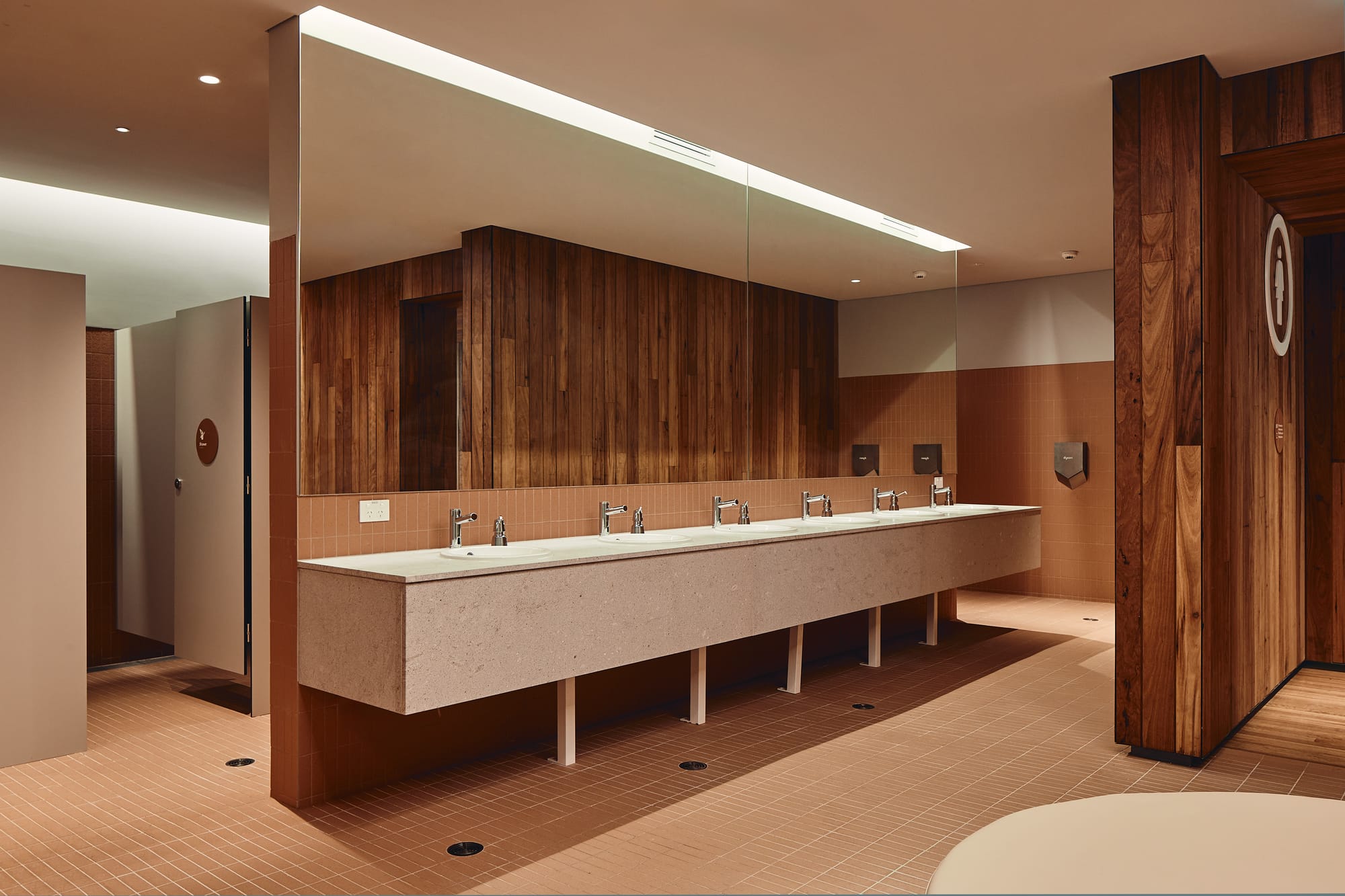 Parramatta Aquatic Centre by Mortlock Timbers. Photography by Peter Bennetts. Bathroom in public pool with tile floors, timber clad walls, concrete bench and large mirrorer wall. 