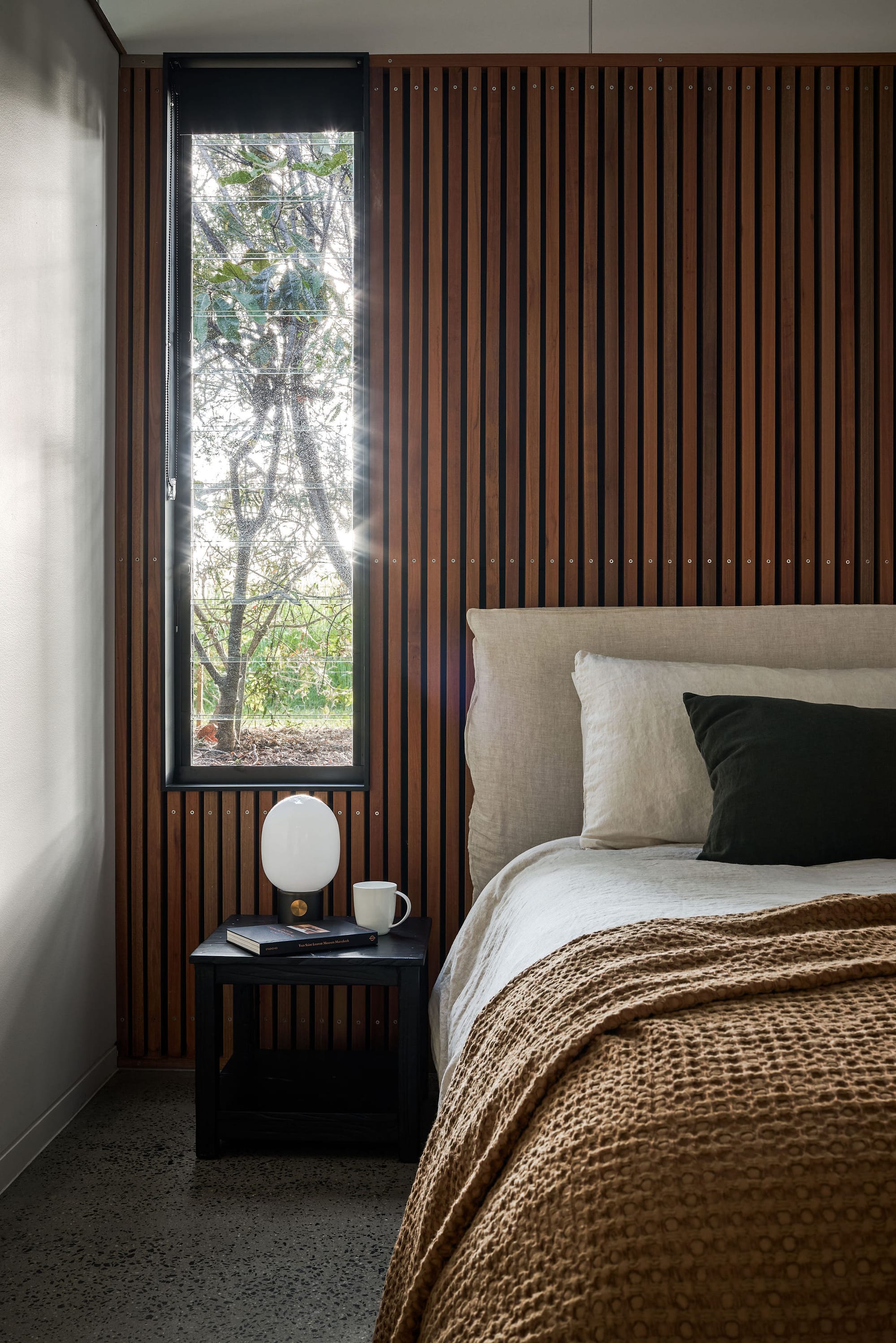 Rockpool Farm Byron Bay. Photography by Andy Macpherson. Bedroom with polished concrete floors and timber clad walls. Mustard waffle throw rug on bed.