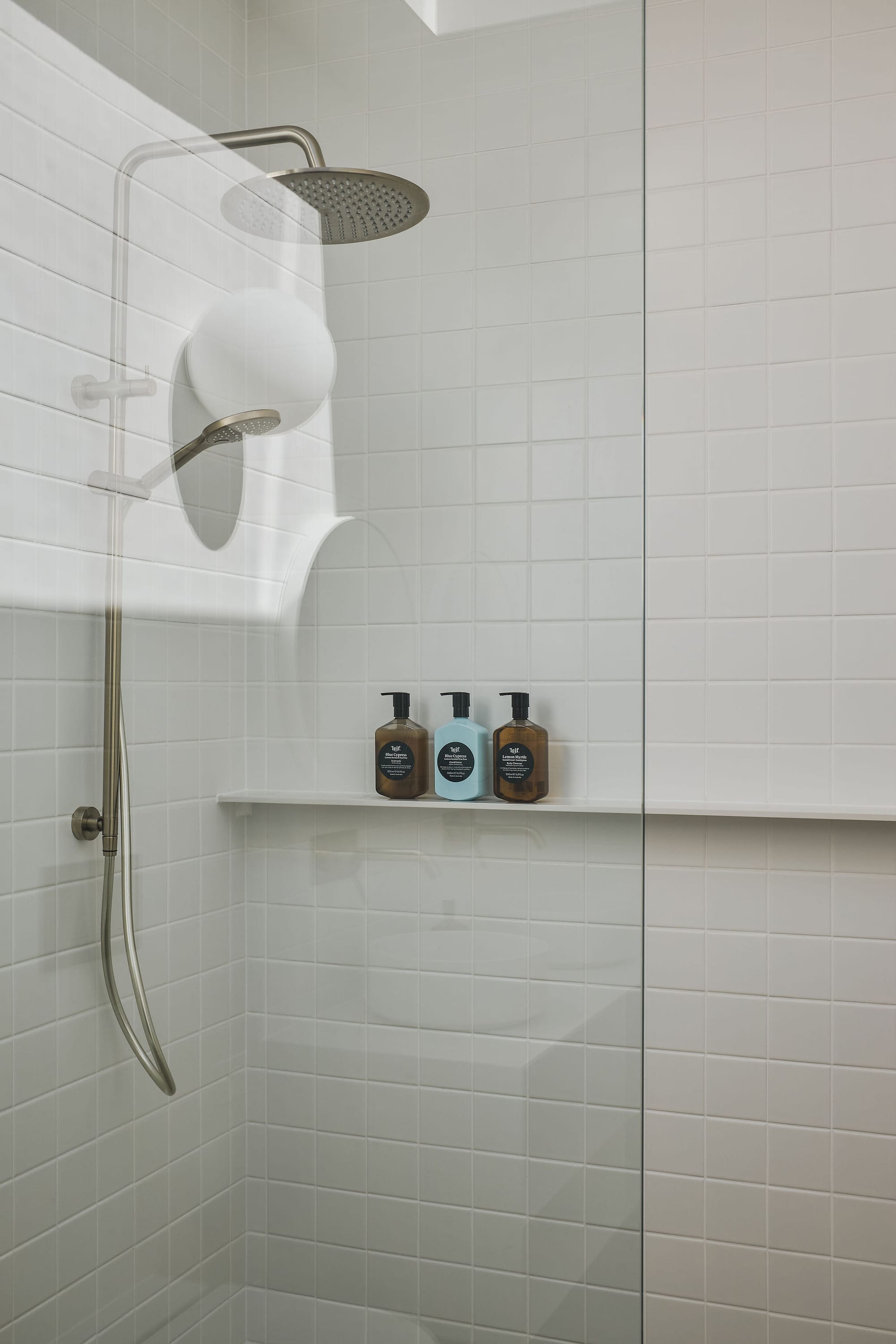 Rockpool Farm Byron Bay. Photography by Andy Macpherson. White tiled bathroom shower with double showerhead and floating white shelf.