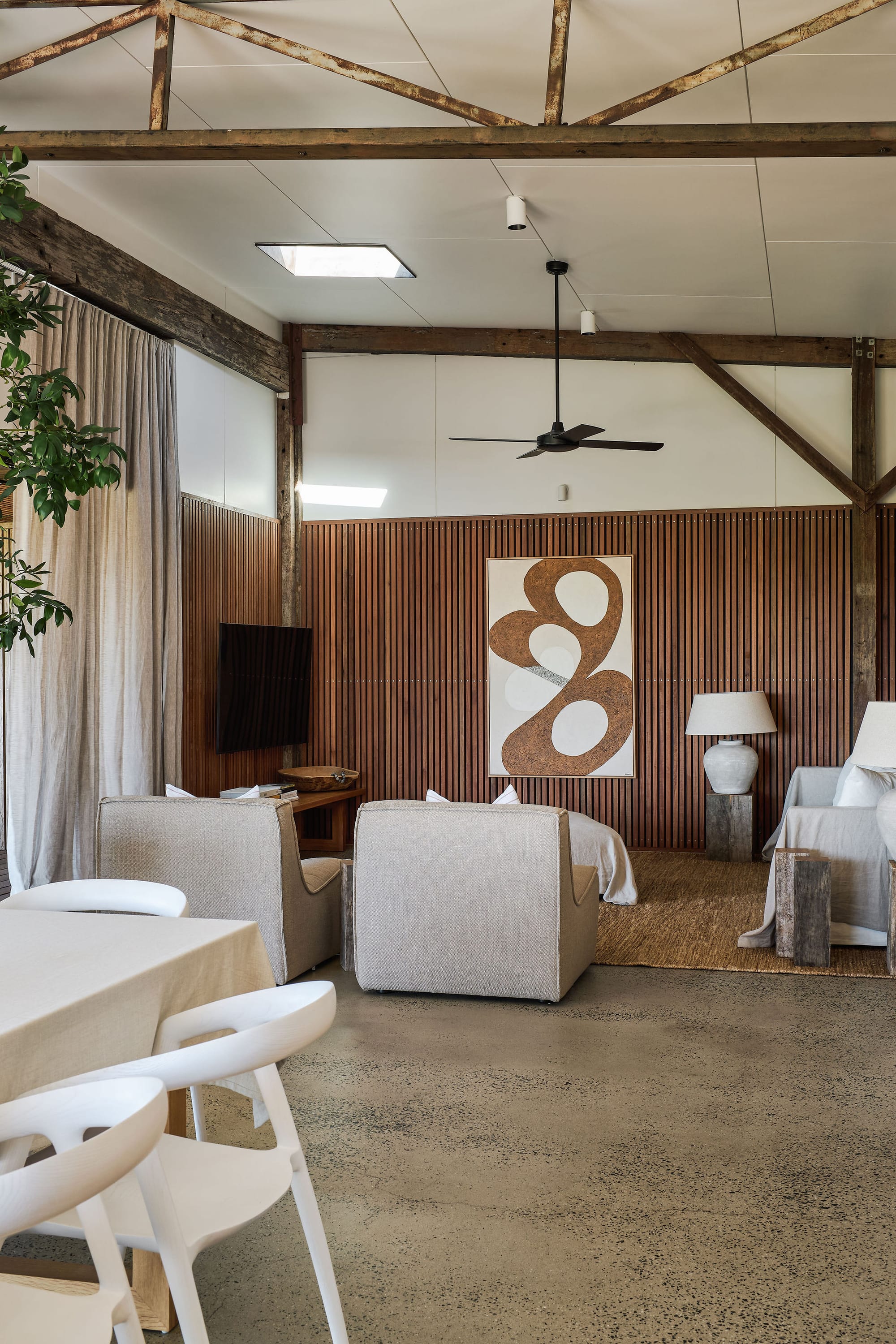 Rockpool Farm Byron Bay. Photography by Andy Macpherson. Open plan living and dining space with polished concrete floors, exposed beams and timber-clad walls. White dining tables, chairs and armchairs.