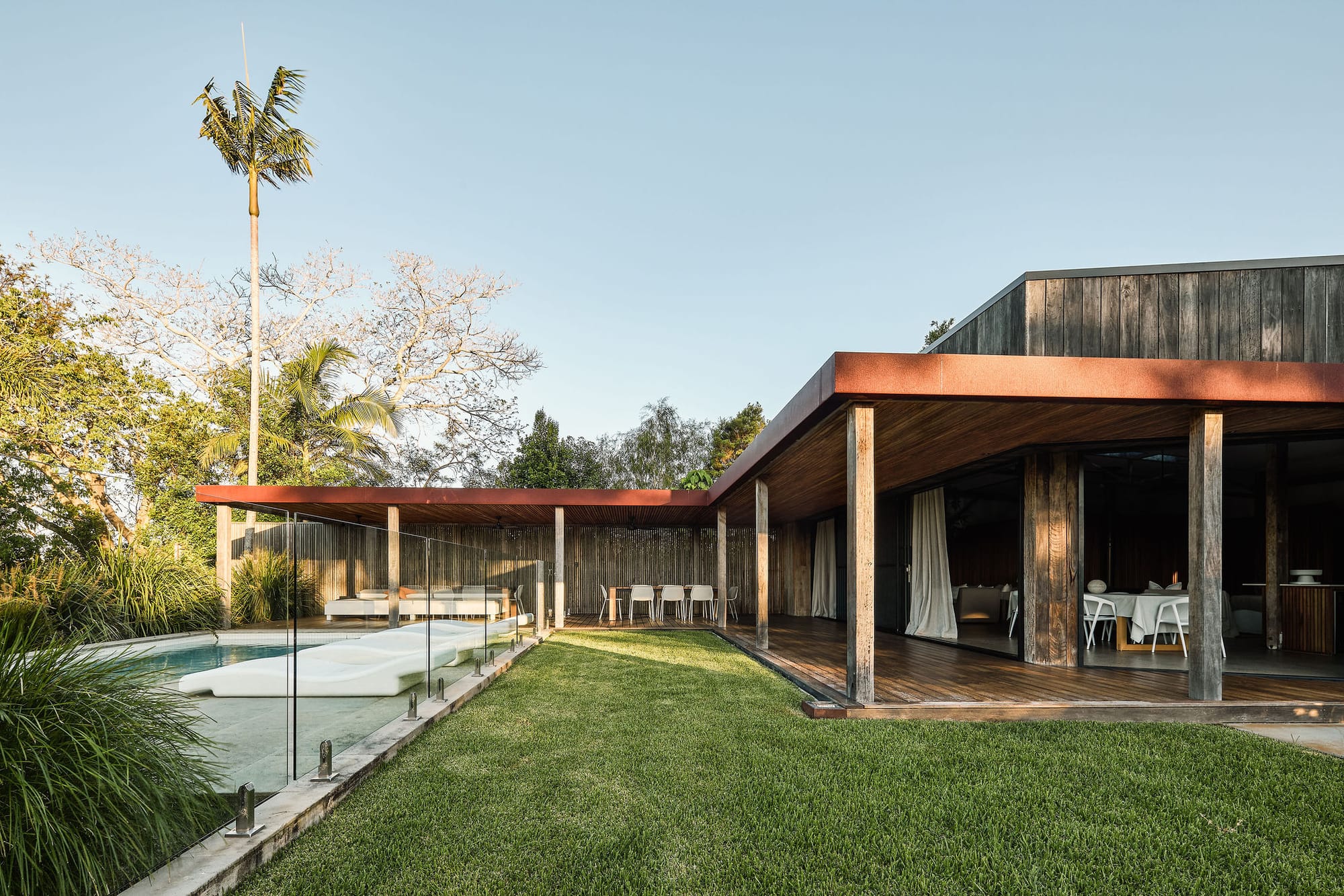 Rockpool Farm Byron Bay. Photography by Andy Macpherson. Timber clad building with timber wraparound deck. Grass between deck and glass pool fence.