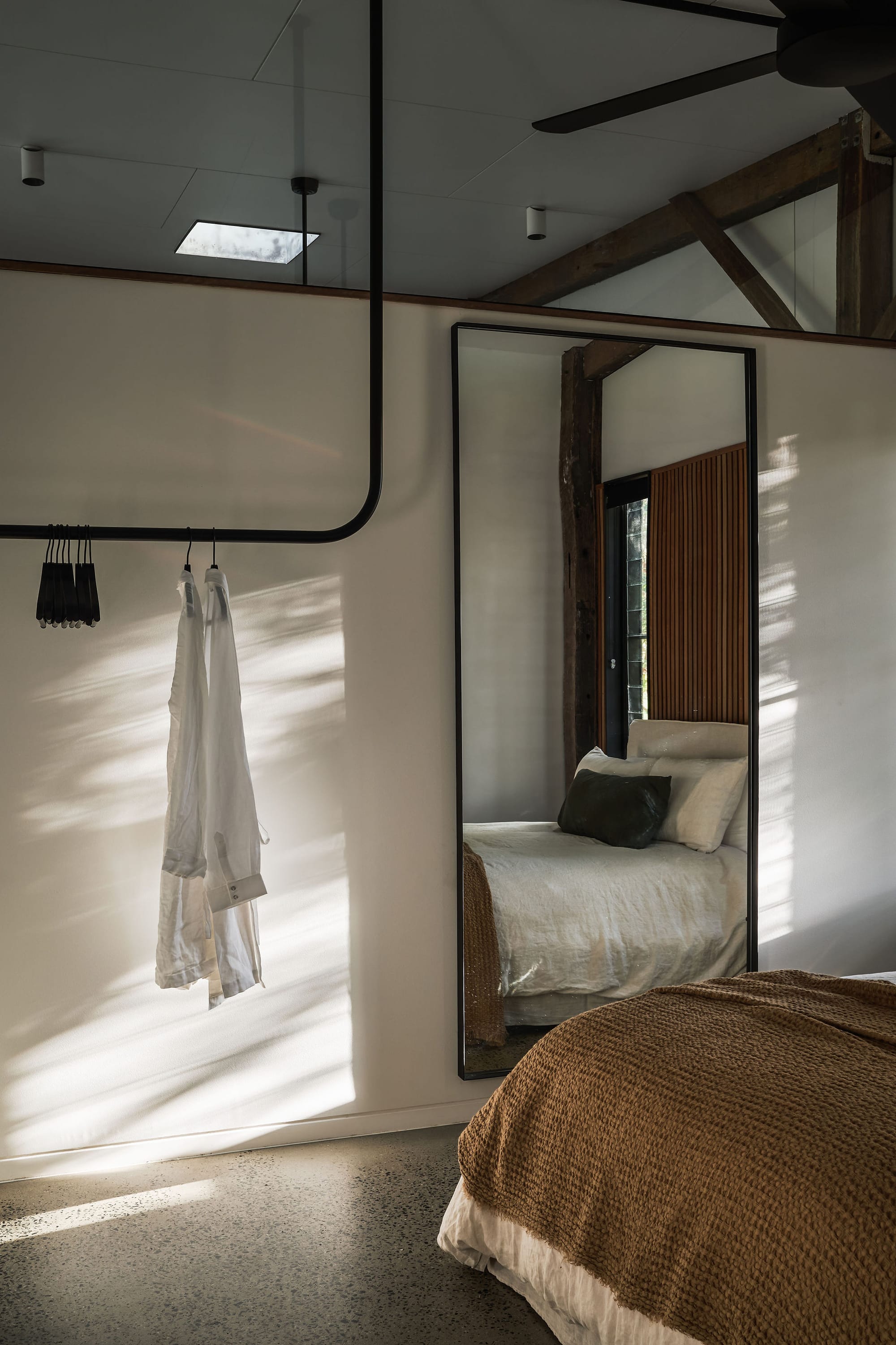 Rockpool Farm Byron Bay. Photography by Andy Macpherson. Bedroom with white walls and polished concrete floors. Bed with mustard throw rug on end. Hanging black framed mirror on wall.