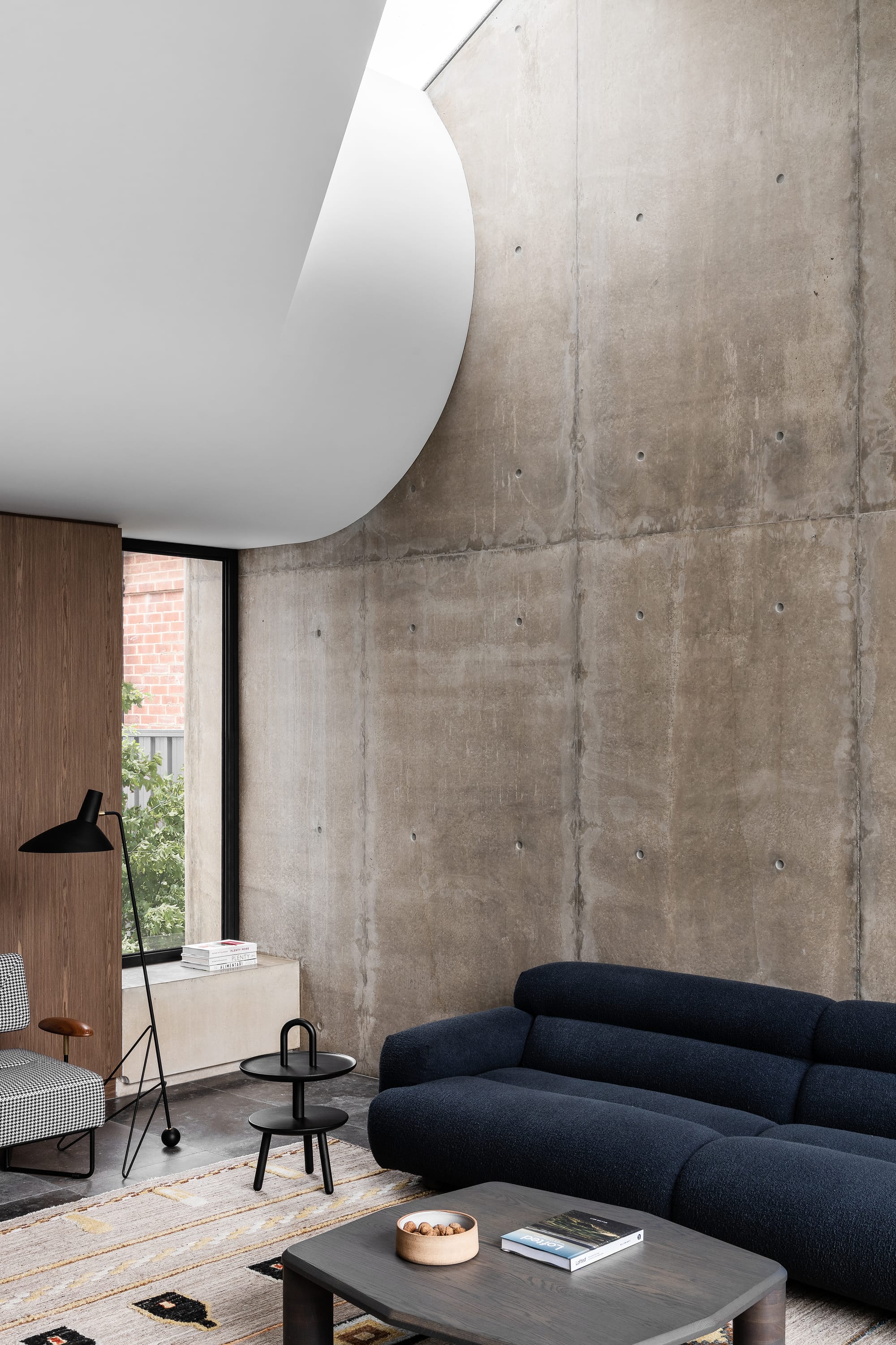 Rose Park by studio gram. Photography by Timothy Ross. Living space with white curved bulkhead. Blue couch and Aztec rug. Concrete walls. 