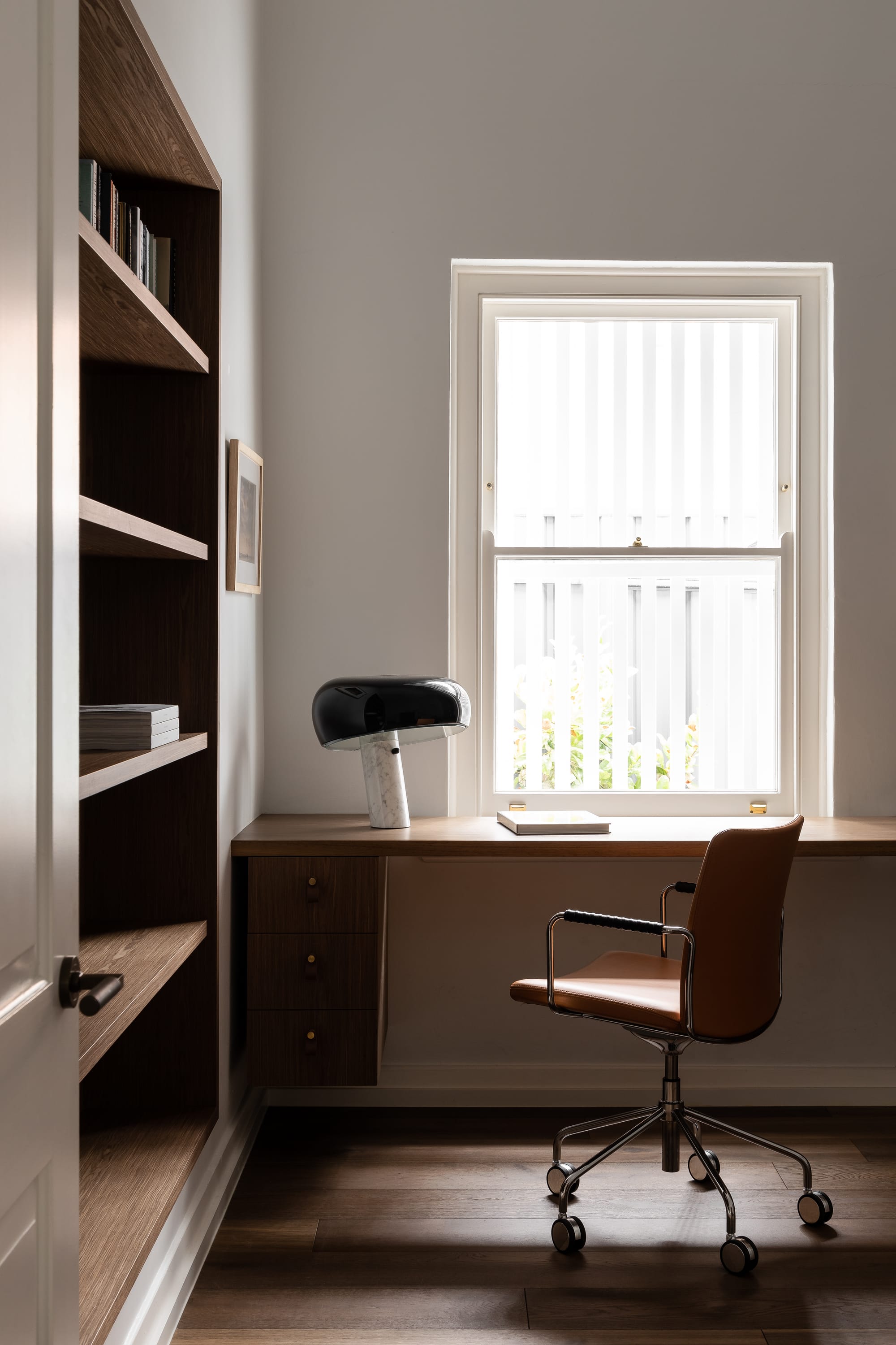 Rose Park by studio gram. Photography by Timothy Ross. Office space in residential home with timber floors, desk and shelving. Orange office chair. White walls and window. 