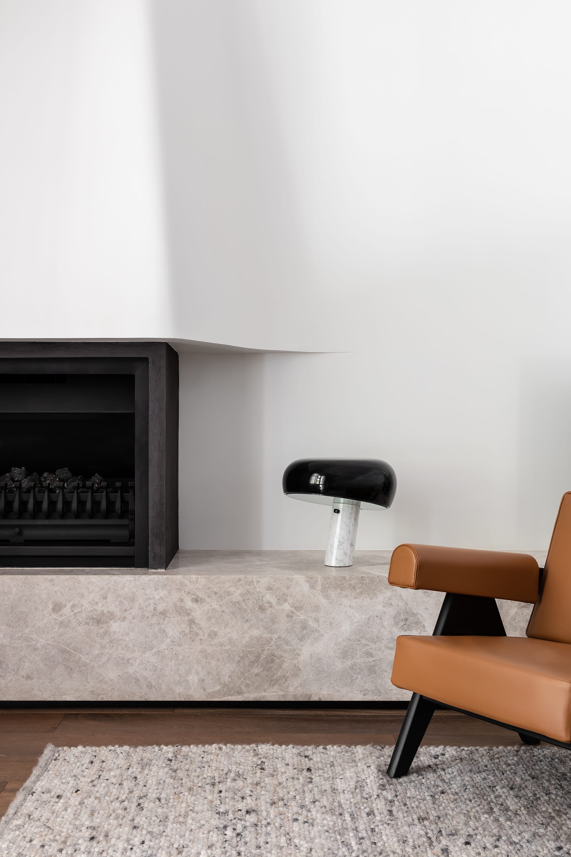 Rose Park by studio gram. Photography by Timothy Ross. Fireplace with light stone hearth. Orange leather armchair to right. Timber floors and white walls. 