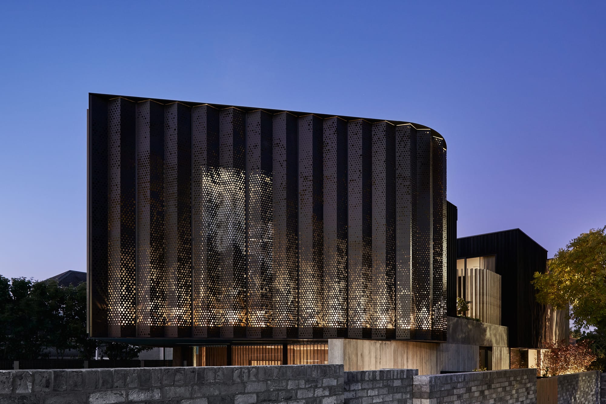 The Split Home by Seidler Group. Copyright of Seidler Group. Perforated metal encased second storey of home from street view at night. Light visible through perforations in metal. 