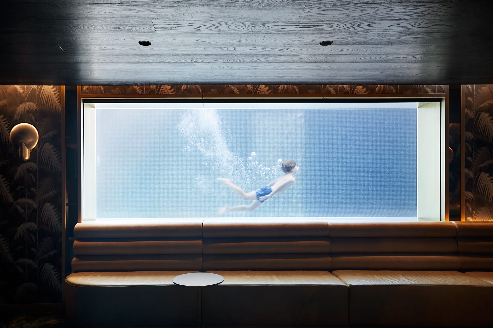 The Split Home by Seidler Group. Copyright of Seidler Group. Lage interior window looking into swimming pool. Child seen swimming in pool. Bench seating runs underneath window. 