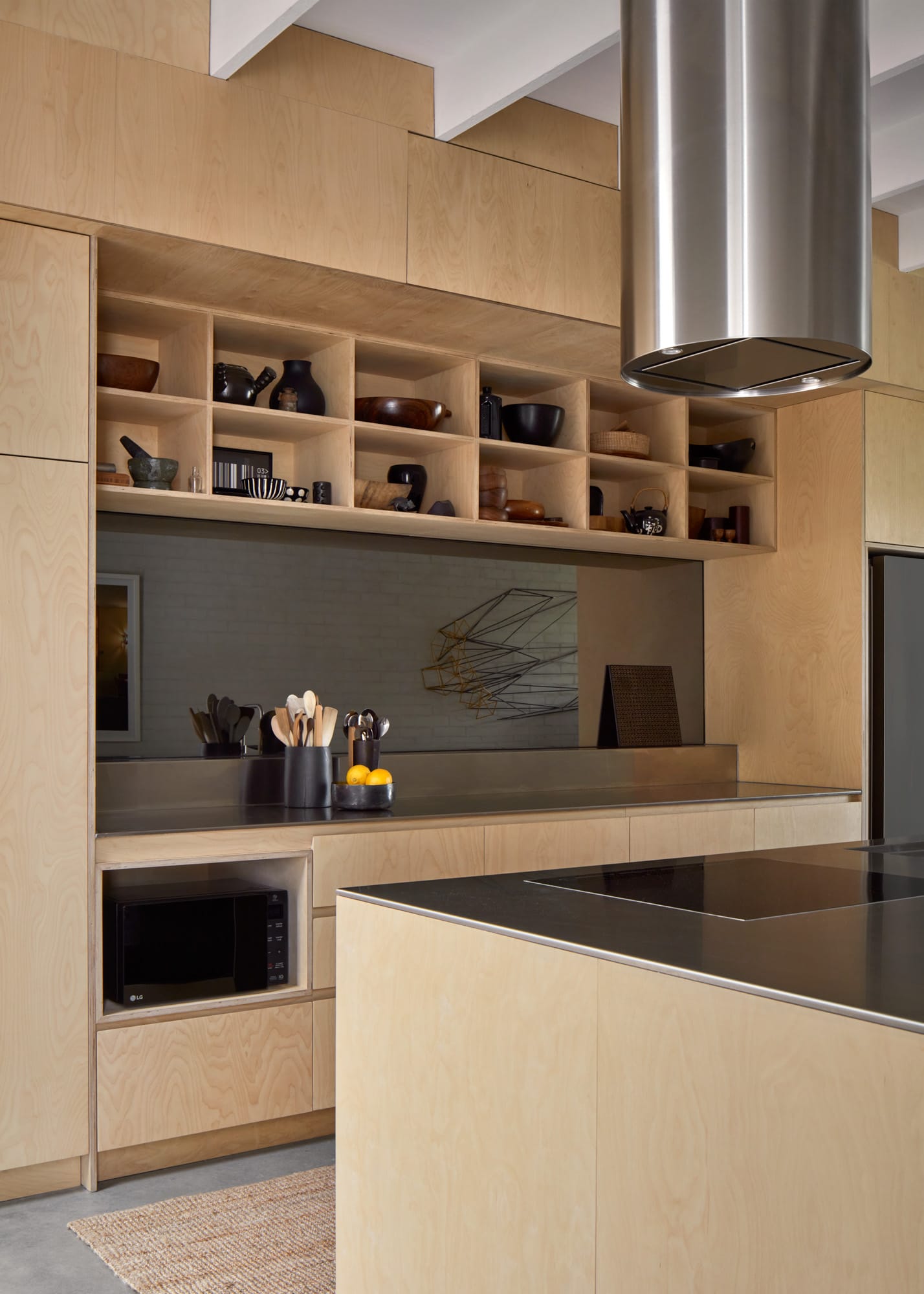 Brick House by Studio Roam. Photography by Jack Lovel. Kitchen with plywood cabinetry and island bench. Aluminum benchtop. Dark reflective splashback. Open overhead storage.  