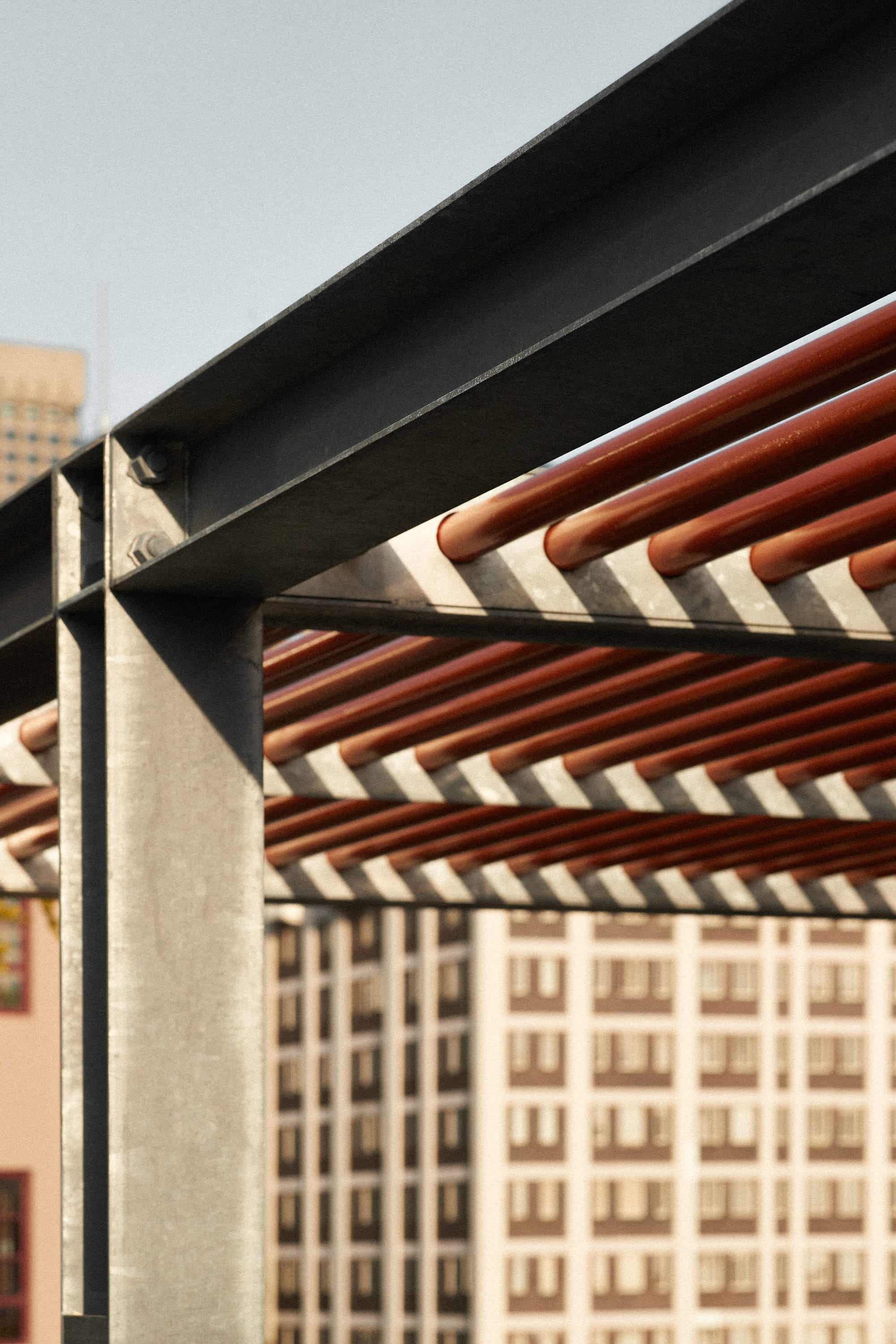 Riley Roof by Studio Shand. Photography by Traianos Pakioufakis. Close up of roof, constructed of aluminum poles and red metal tubes running horizontally. 