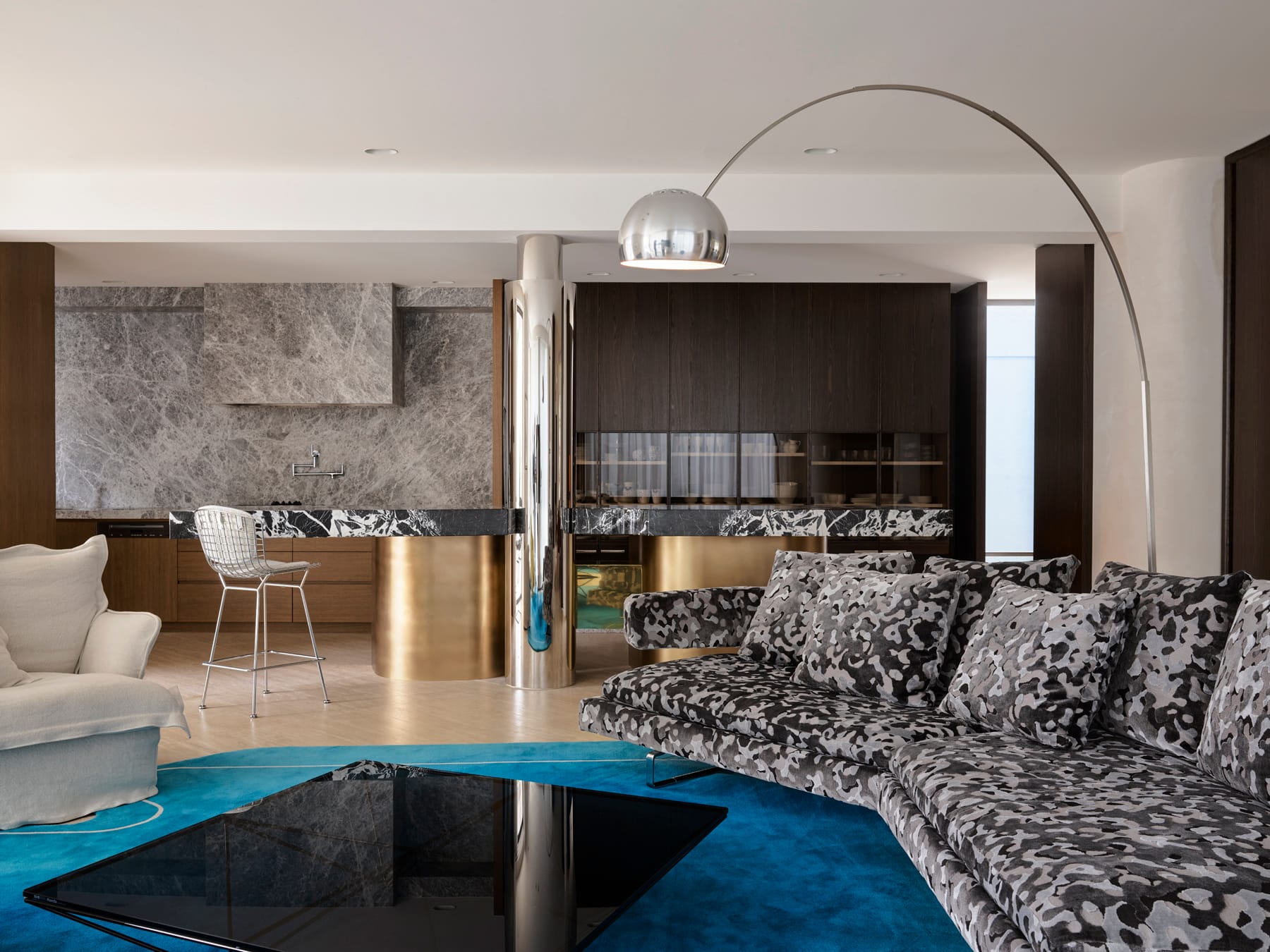 Toorak House 2 by K.P.D.O. Photography by Sharyn Cairns. Abstract print couch with electric blue rug. Gold, black and stone kitchen in background. Large black coffee table. 