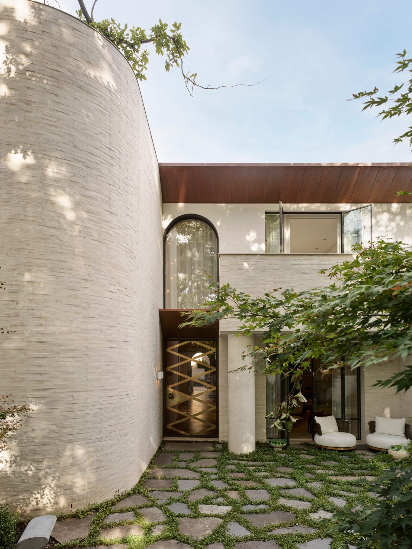 Toorak House 2 by K.P.D.O. Photography by Sharyn Cairns. Front facade and entry to double storey home. White curved brick wall. Gold abstract front door. Grass growing between pavers. 
