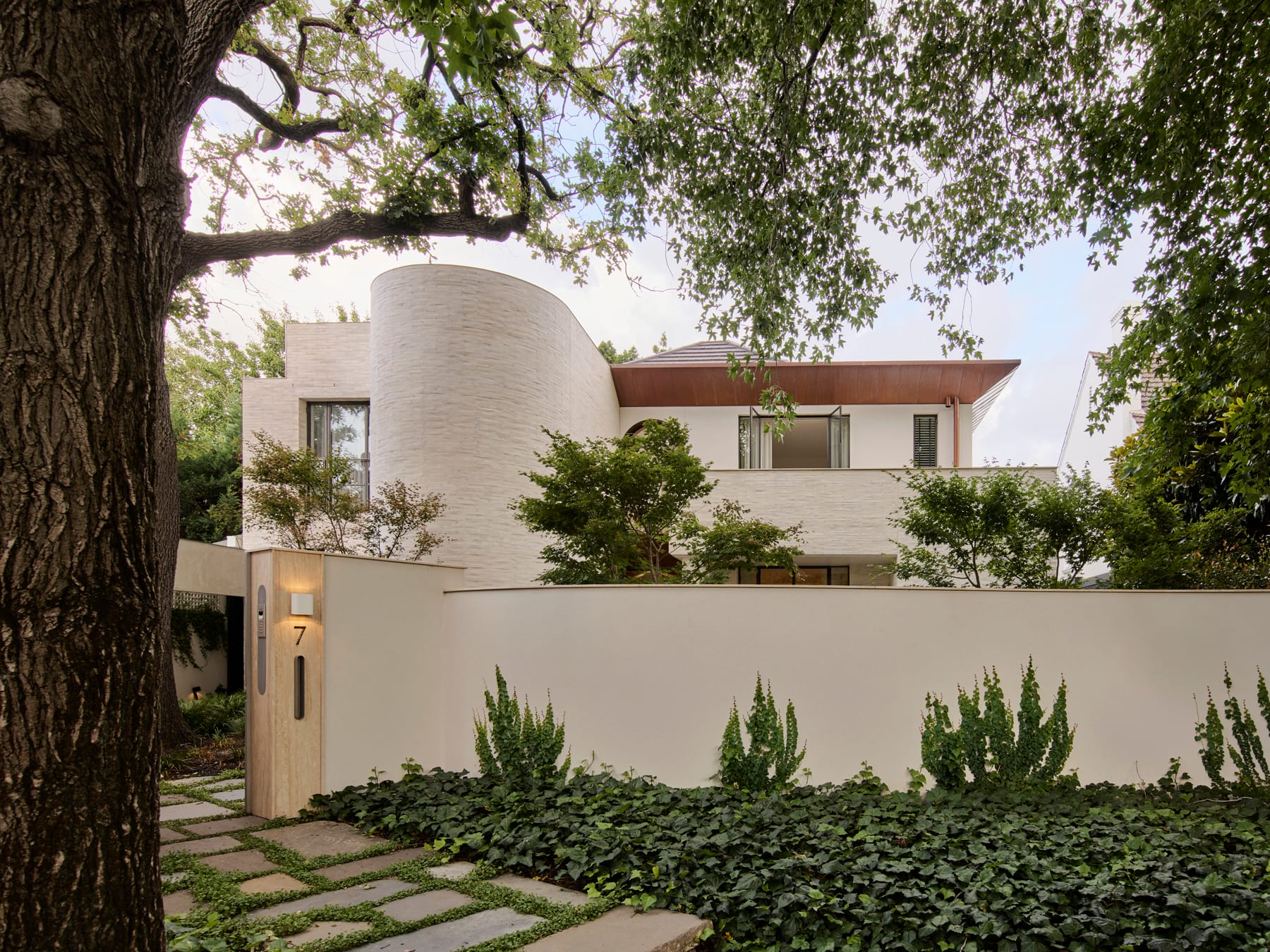 Toorak House 2 by K.P.D.O. Photography by Sharyn Cairns. Street view of double storey white brick home. Lots of greenery on street verge and behind front curved fence.