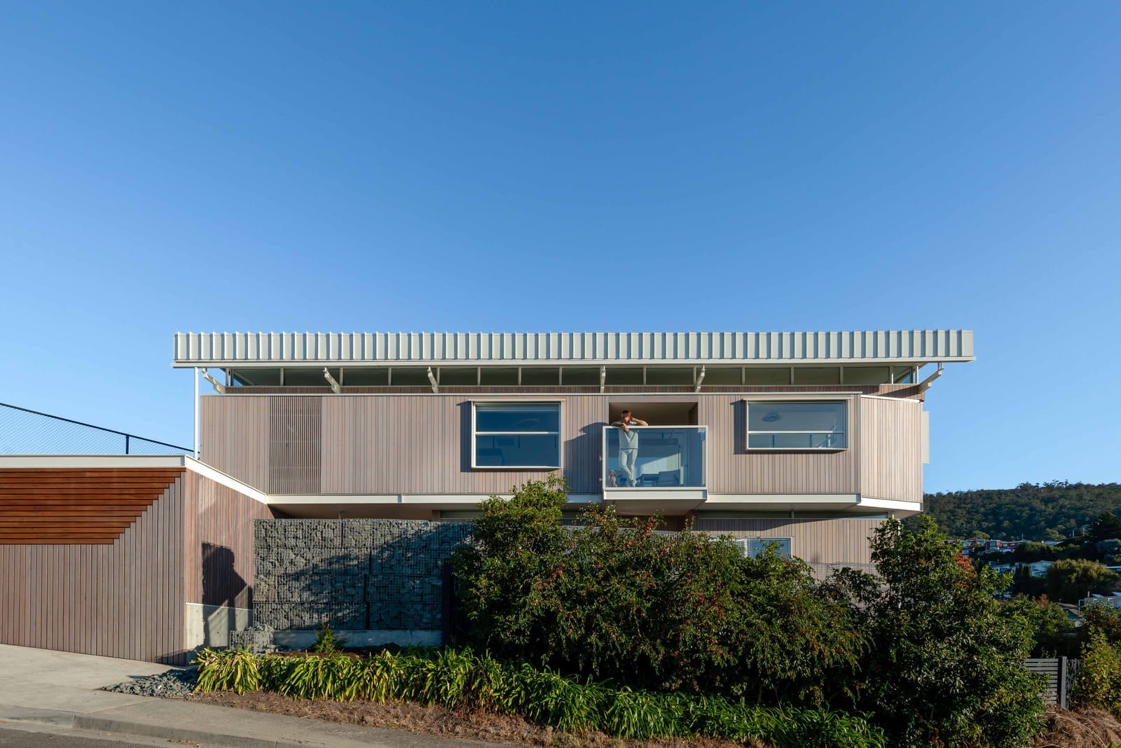 Wattle Bird House by Flett Architecture. Photography by Matt Sansom. Timber clad double storey home on hill. Glass balcony overlooking street. 