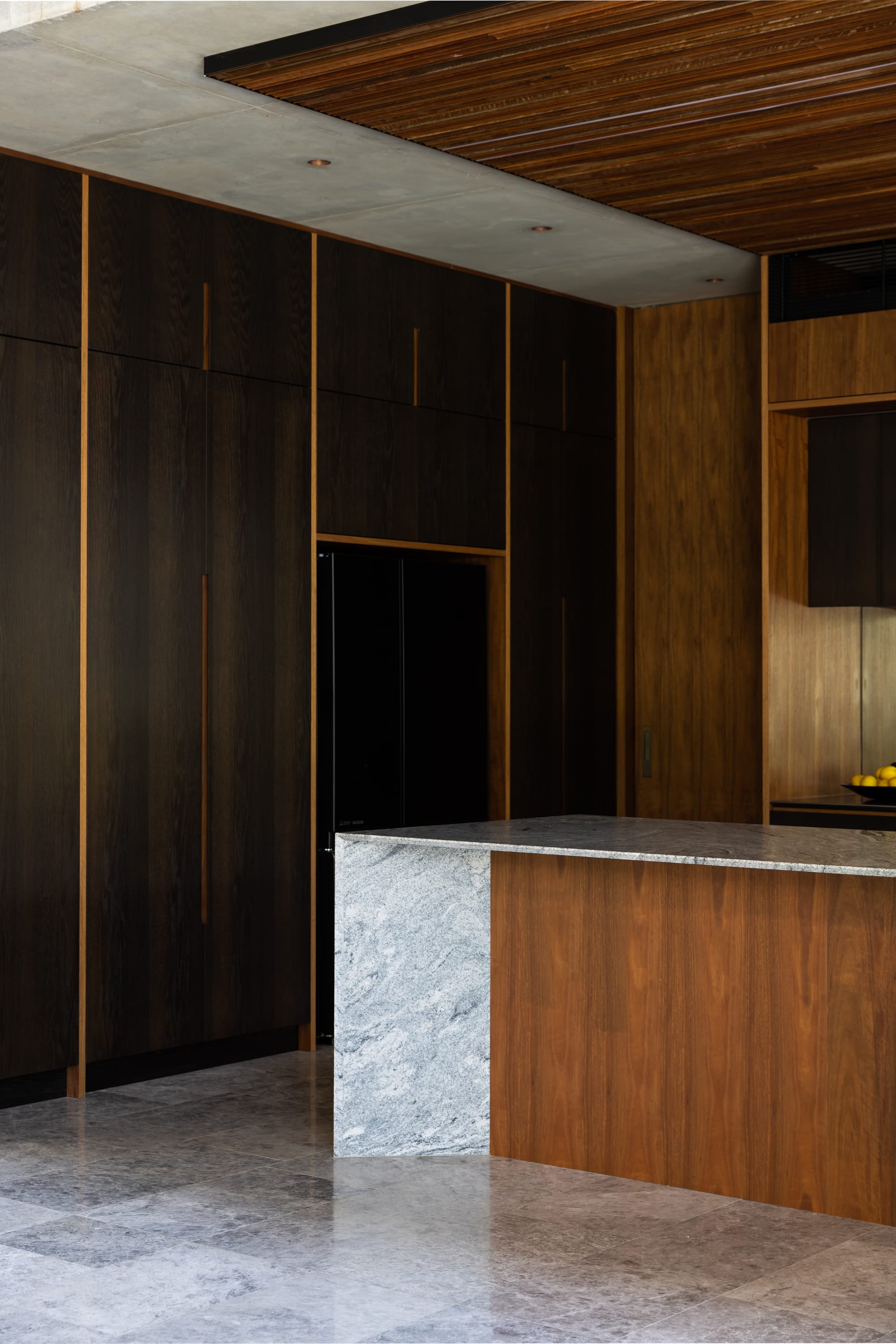 Mortlock Timbers Series: Fox Valley House. Photography by Simon Whitbread. Kitchen with marbled granite floors and timber cabinetry. Warm timber island bench, dark timber veneer cabinetry to left.