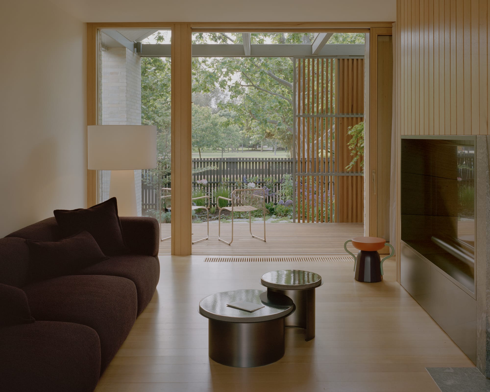 Gable Park by Weaver+Co Architects. Photography by Tasha Tylee. Living space with timber floors, timber framed doors and windows and timber clad feature wall. Burgundy boucle couch. Opens onto verandah with garden views. 