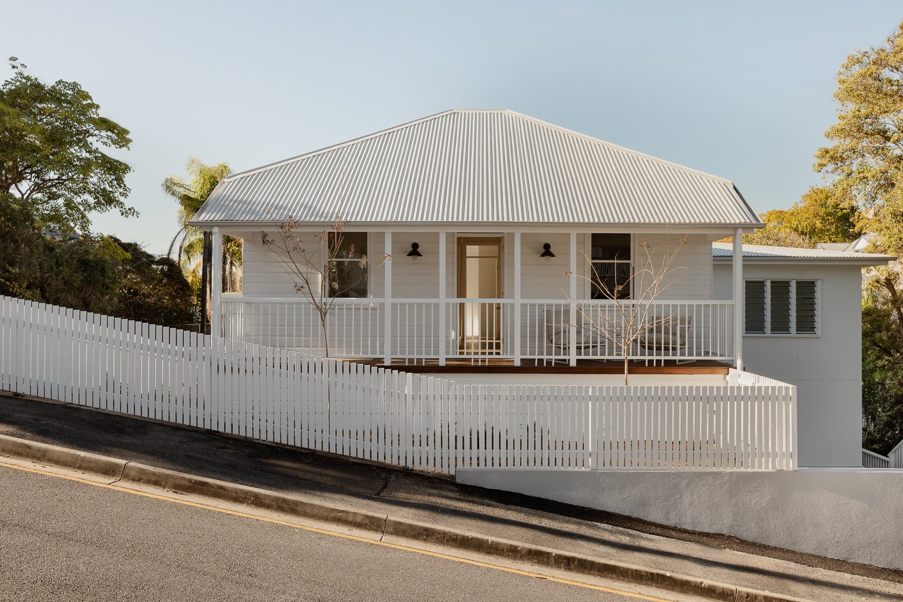 Hazlewood House by Favell Architects. Photography by Andy Macpherson. Street facade of front of white timber clad renovated cottage. Steep hillside street stretching up to left of image.